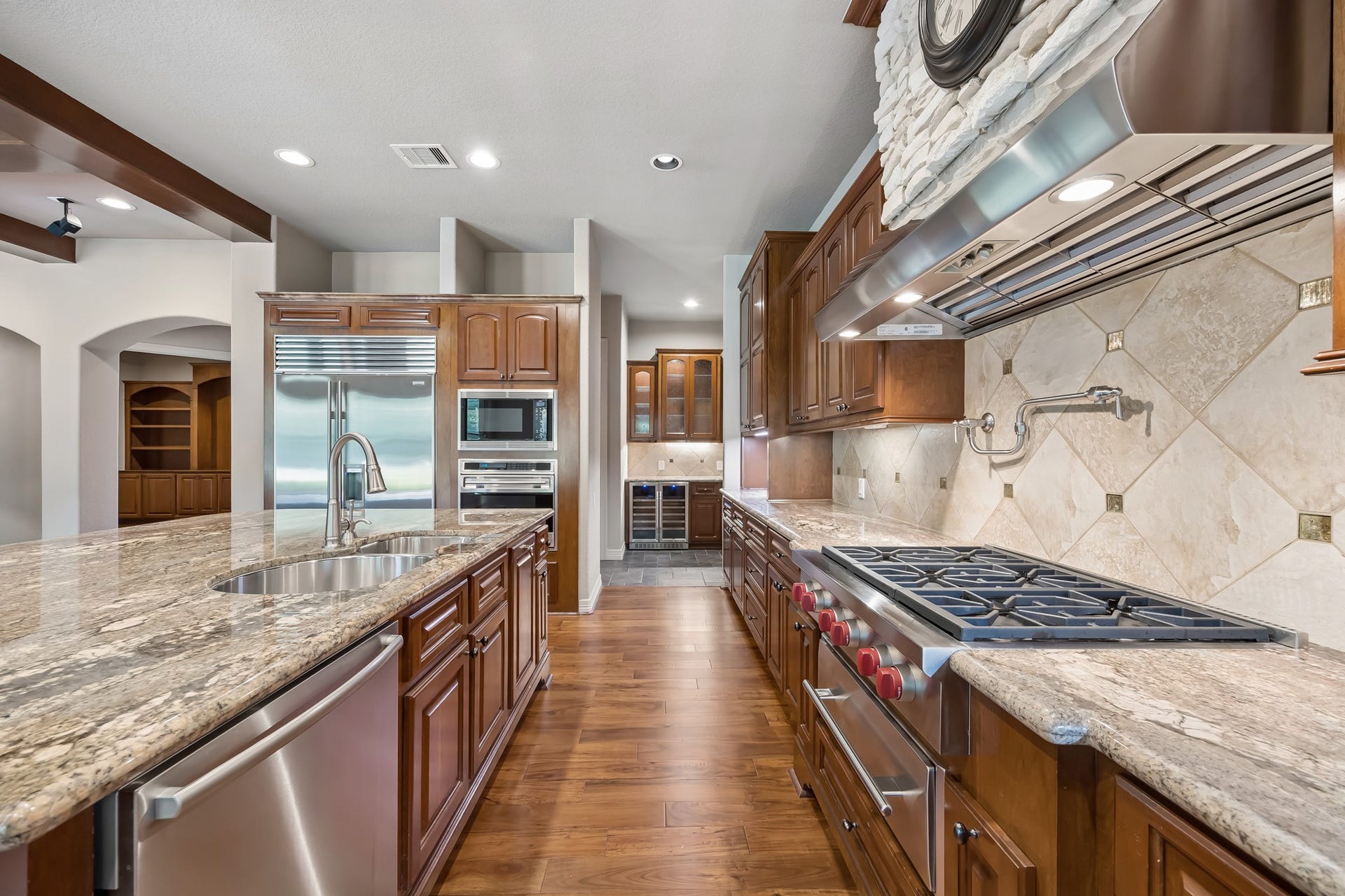 Spacious gourmet kitchen featuring elegant granite countertops, high-end stainless steel appliances, wine refrigerator and rich wooden cabinetry, perfect for culinary enthusiasts.