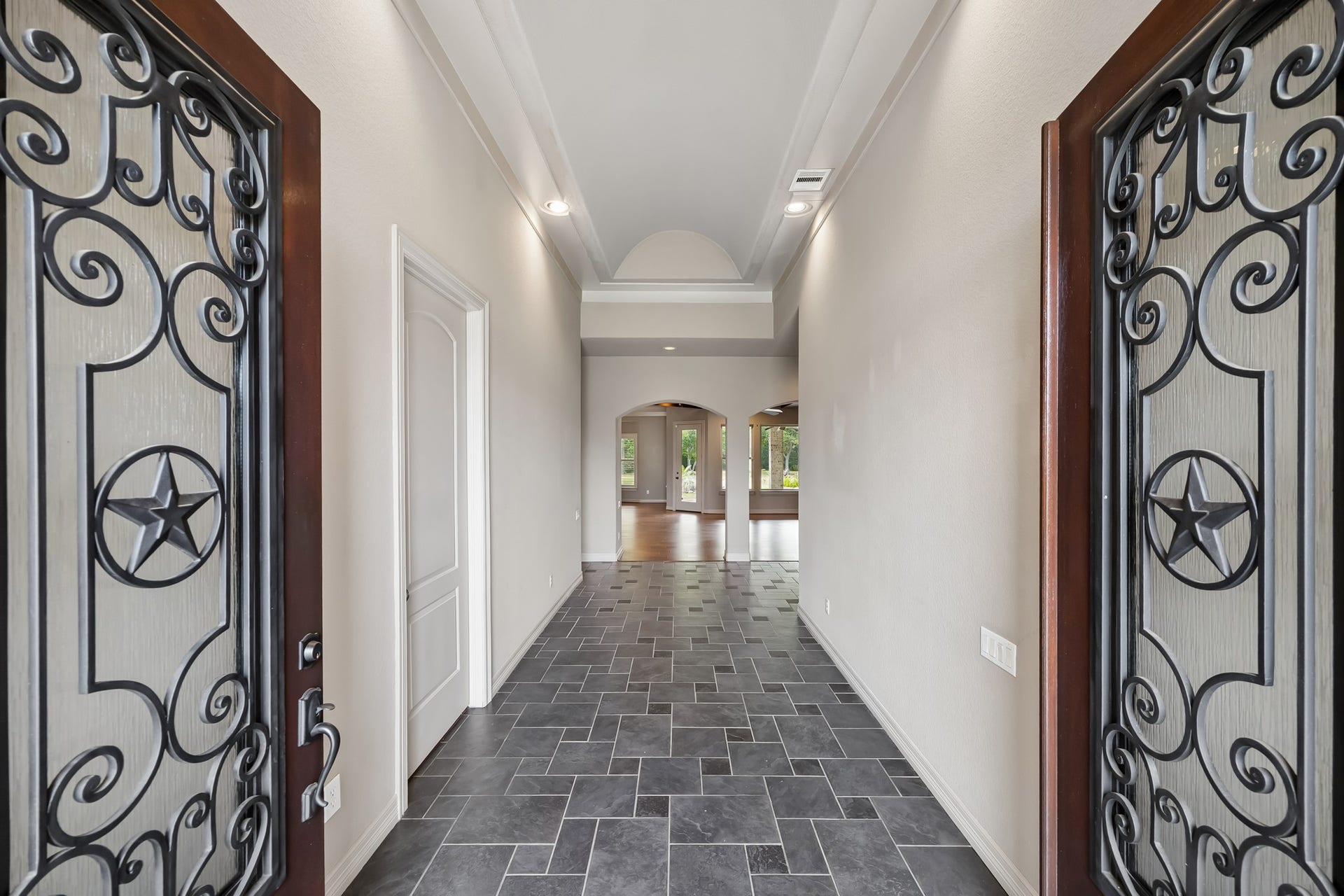 Elegant entryway featuring decorative wrought iron double doors, leading to a spacious, light-filled hallway with sleek tiled flooring and high ceilings.