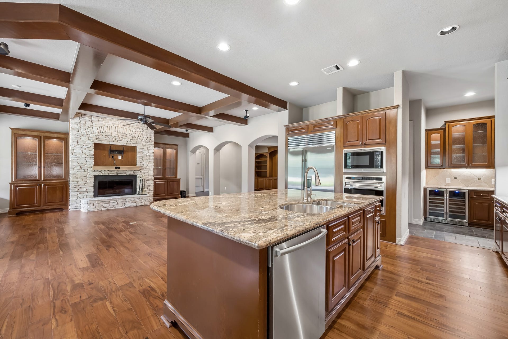 Spacious open-concept kitchen and living area featuring elegant wood-beamed ceilings, a large stone fireplace, and a central island with granite countertops, perfect for entertaining.