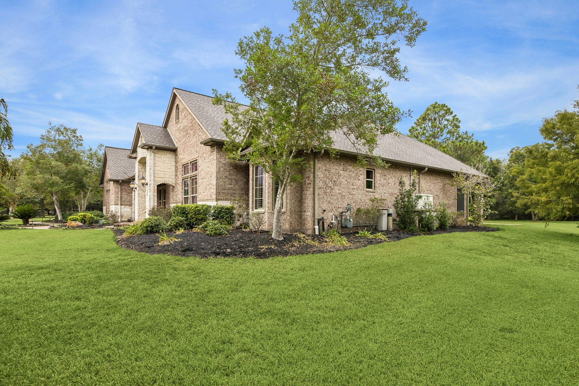 A beautiful brick home surrounded by lush greenery, featuring elegant architectural details and a spacious lawn with sprinkler system located around the home.