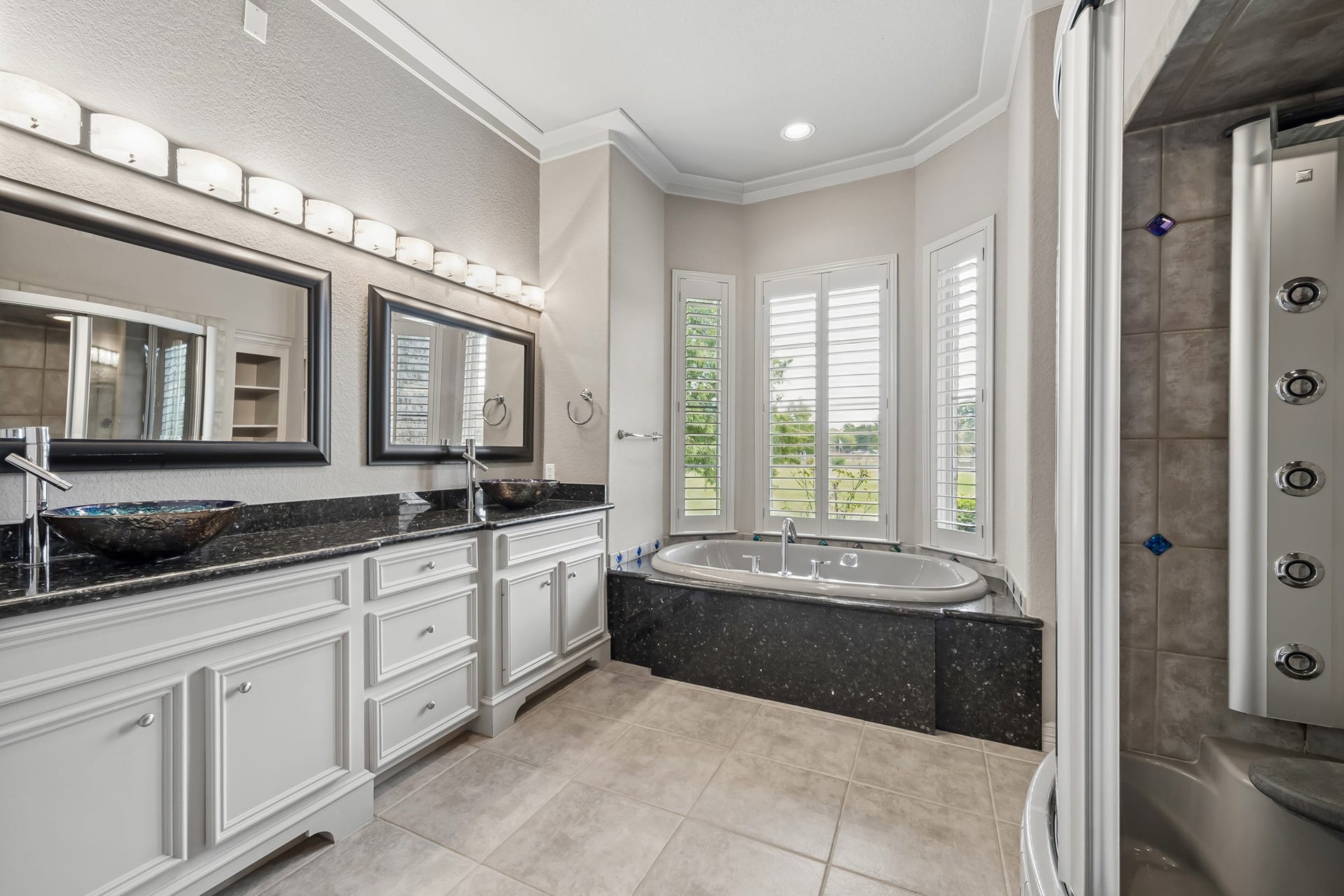 Luxurious bathroom featuring a sleek double vanity with vessel sinks, a relaxing corner jetted tub framed by bright windows, and a modern shower with multiple jets.