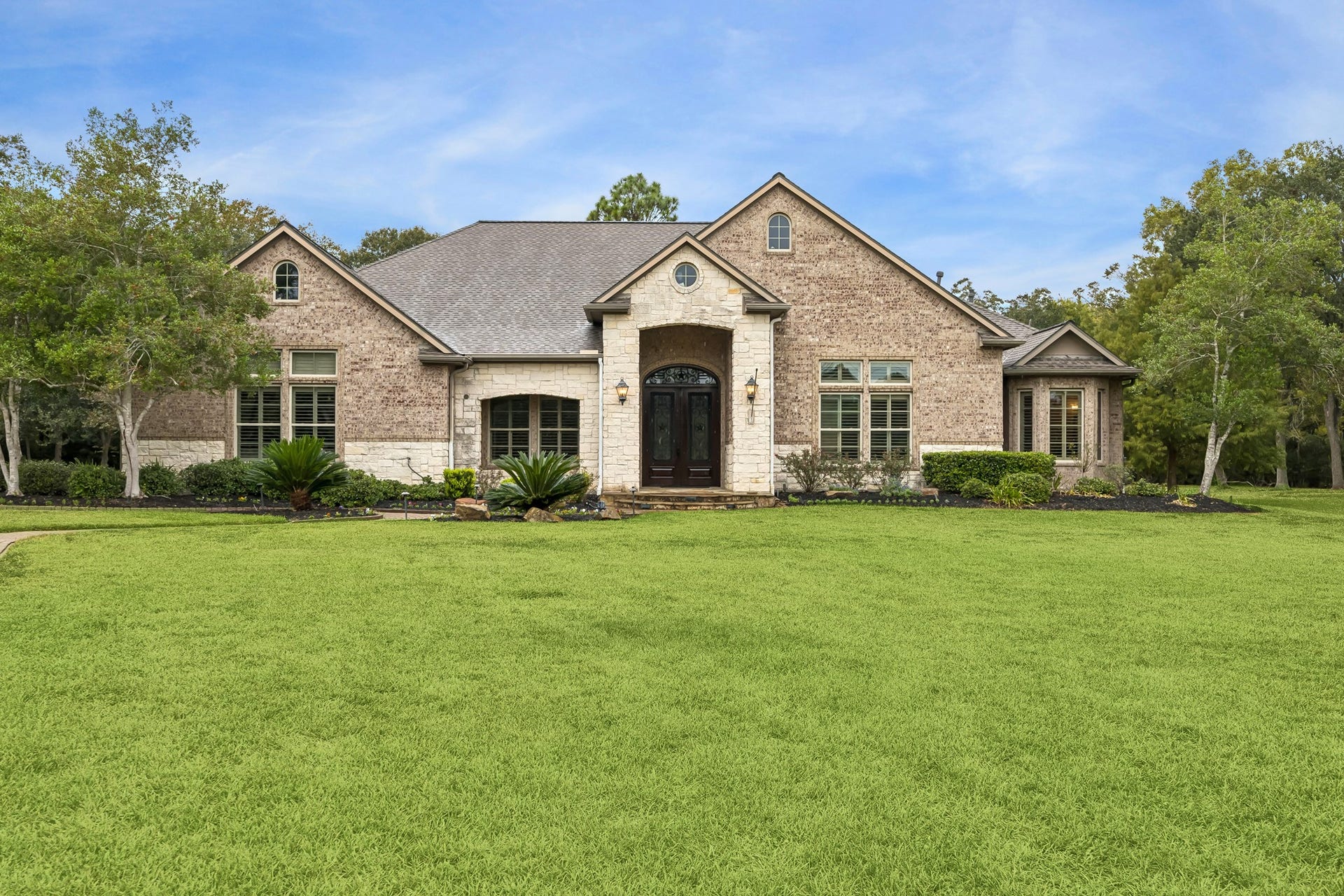 Charming brick home with elegant arched entry, surrounded by lush greenery and mature trees, offering serene suburban living.