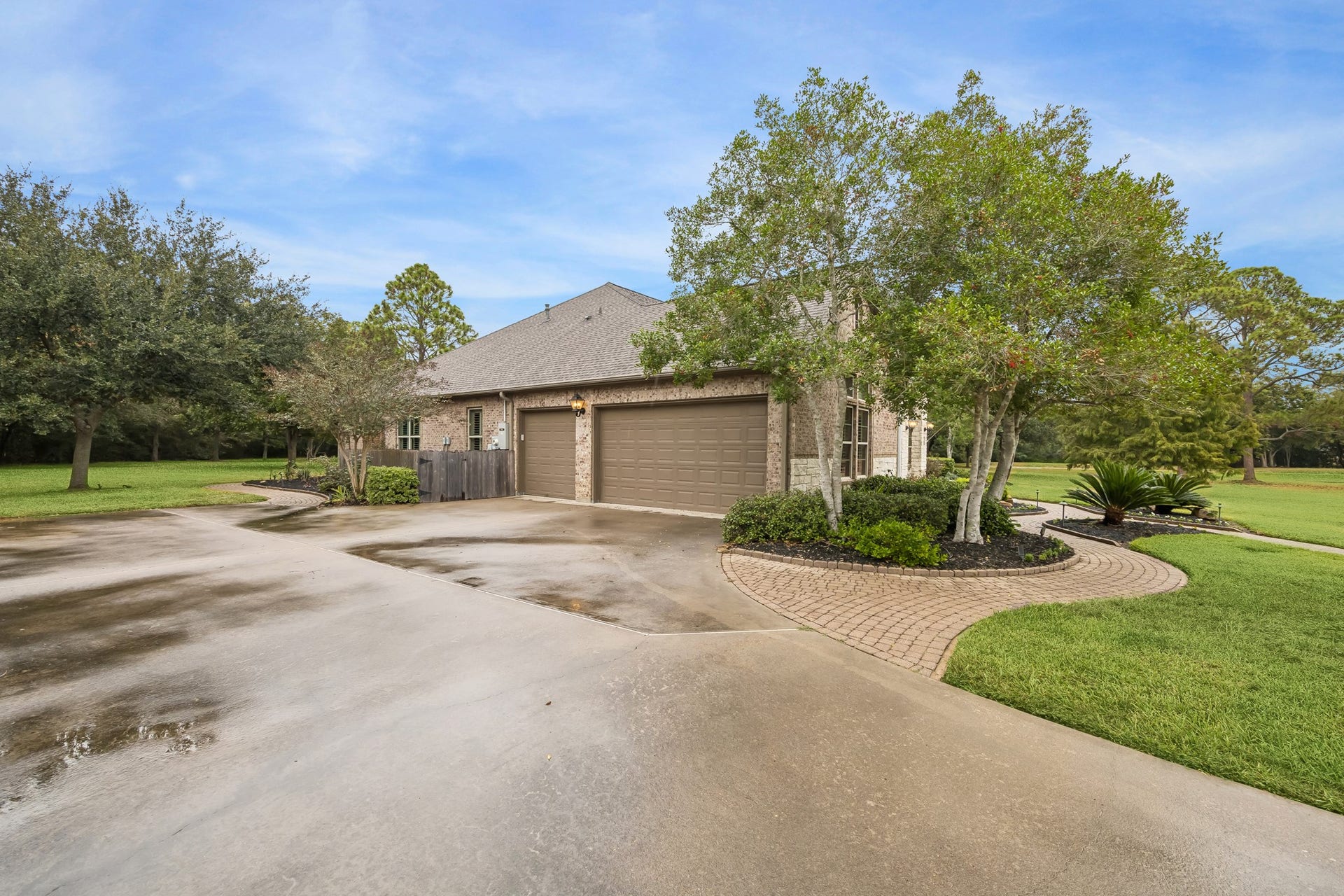Charming brick home with a spacious driveway, lush landscaping, and a three-car garage.