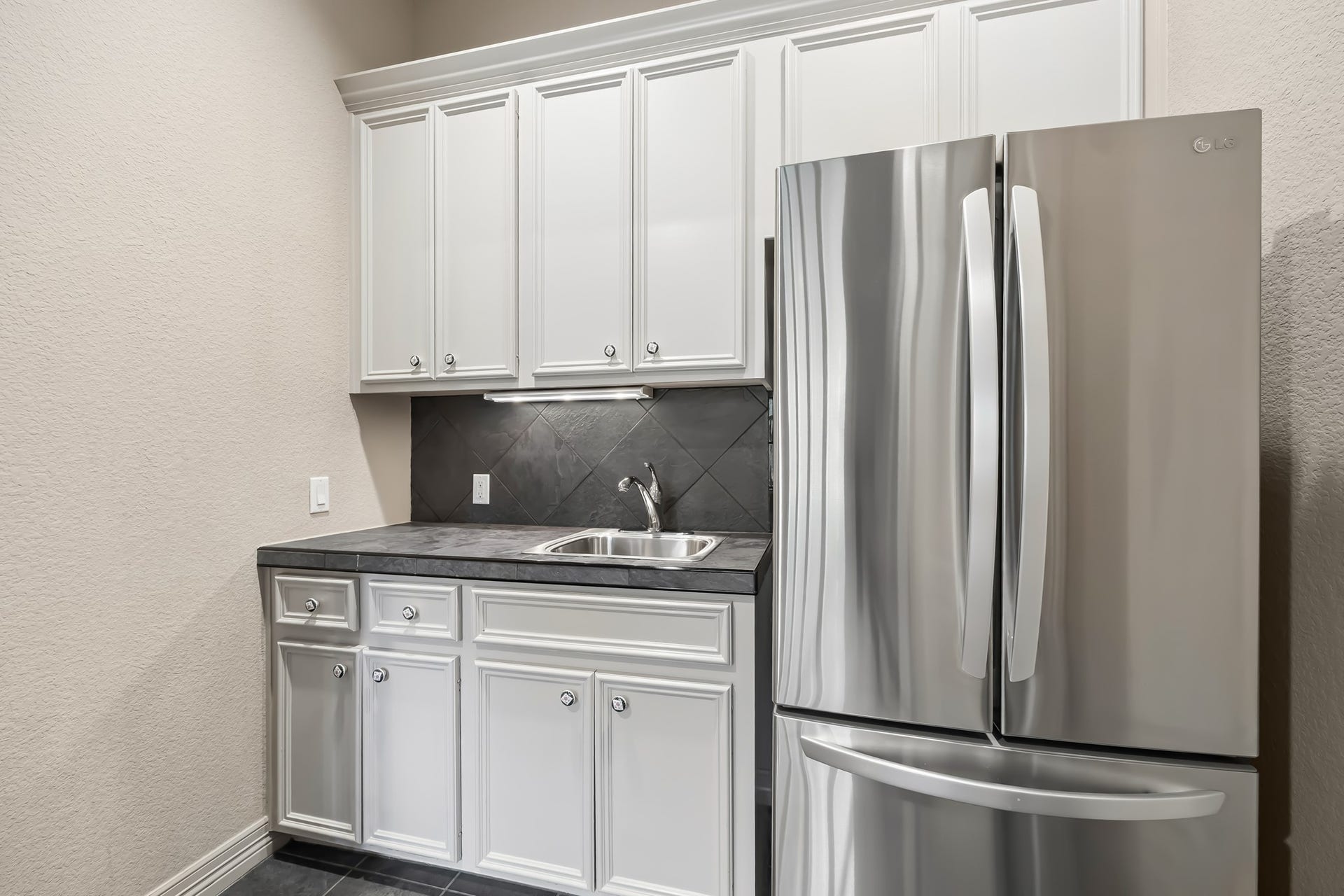 Modern utility space featuring sleek stainless steel appliances, ample white cabinetry, and a convenient sink area for added functionality.  Kitchenette