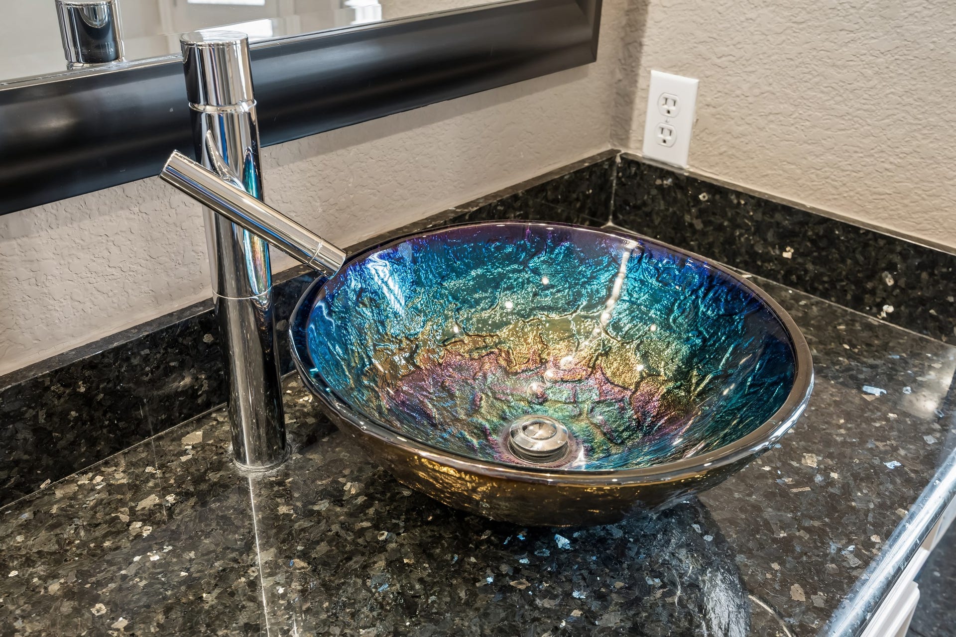 Stunning iridescent vessel sink with a sleek chrome faucet, set against a luxurious dark granite countertop.