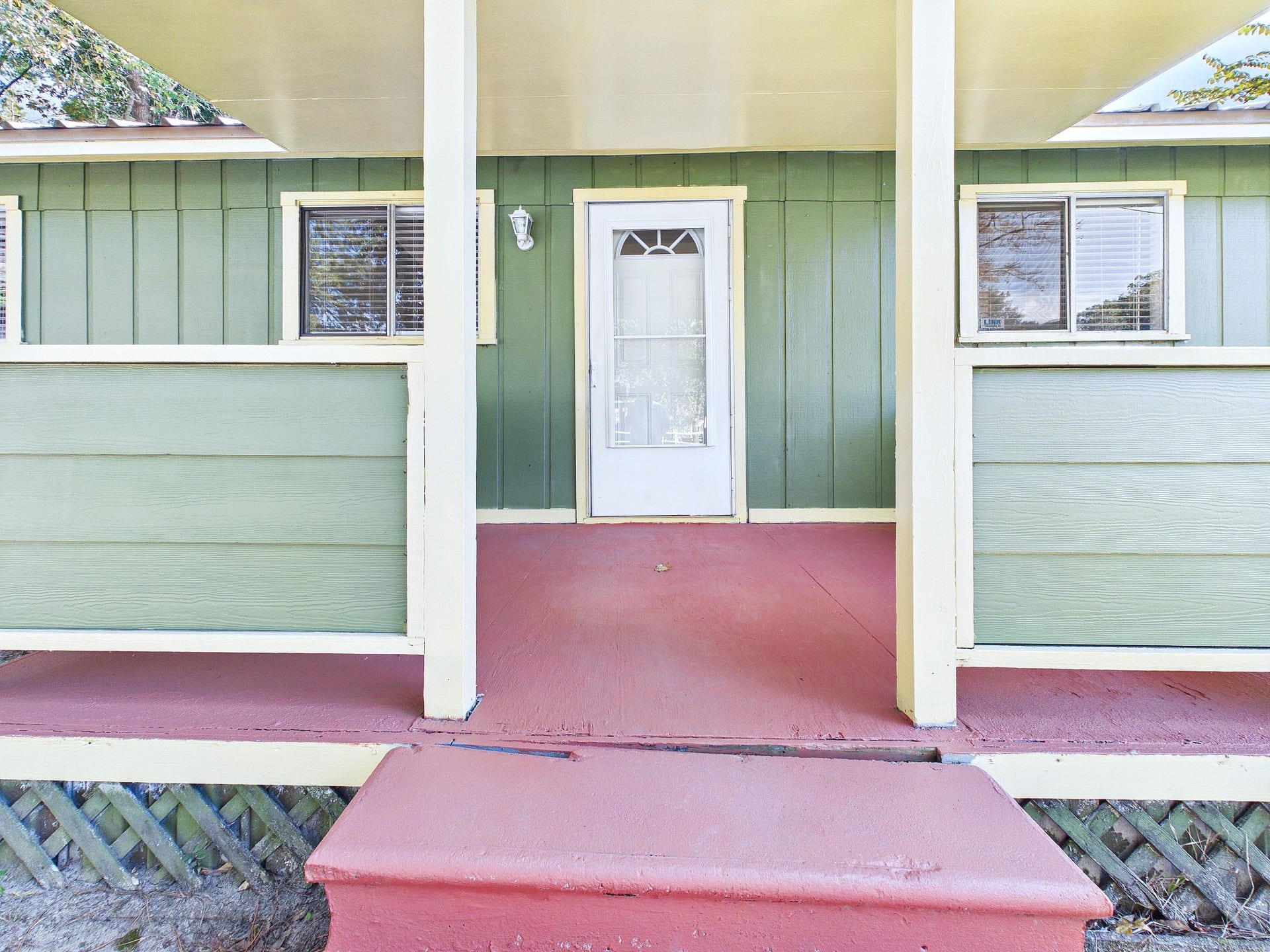 22054 Spears Road, Porter, TX 77365 Charming home entrance with a welcoming covered porch, featuring vibrant green siding and contrasting red flooring, perfect for relaxing outdoors.