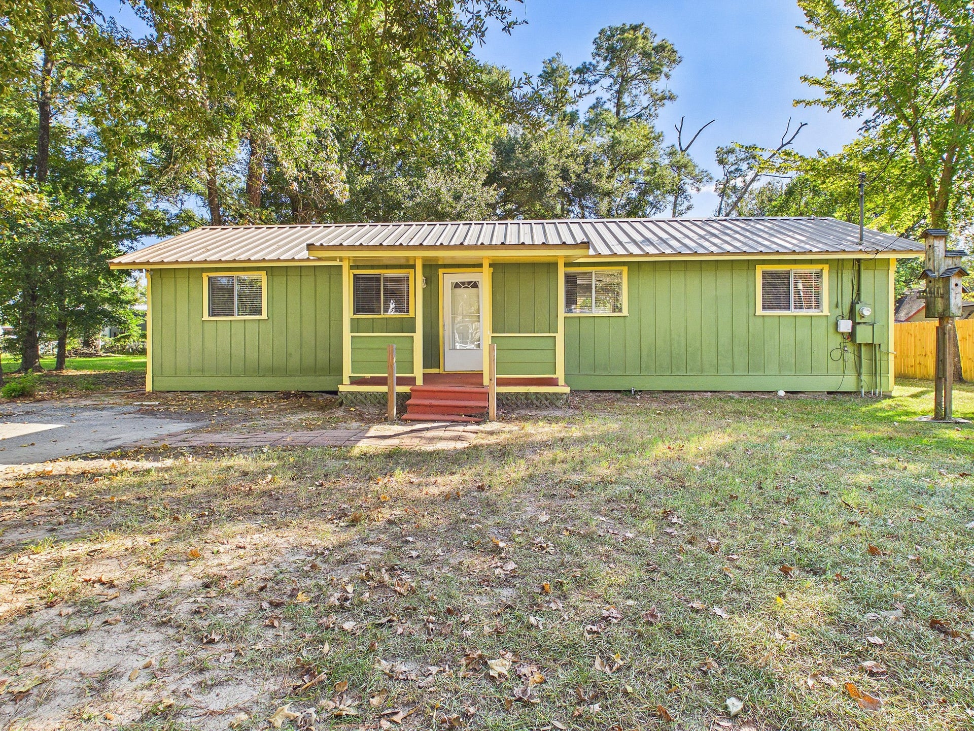 22054 Spears Road, Porter, TX 77365 Charming single-story home with a bright green facade, metal roof, and cozy front porch, surrounded by mature trees in a serene setting.