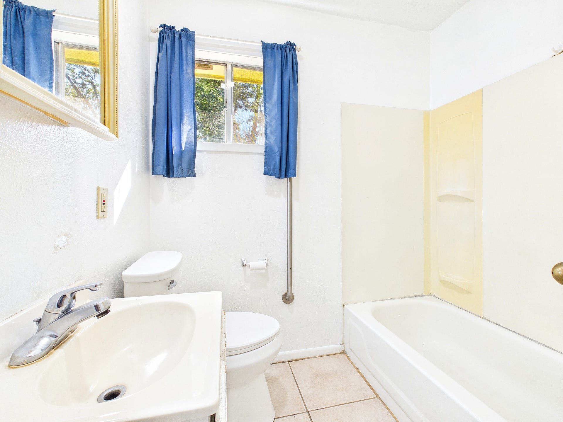 22054 Spears Road, Porter, TX 77365 Bright bathroom featuring a clean white sink, bathtub, and toilet, complemented by blue curtains and a convenient window for natural light.