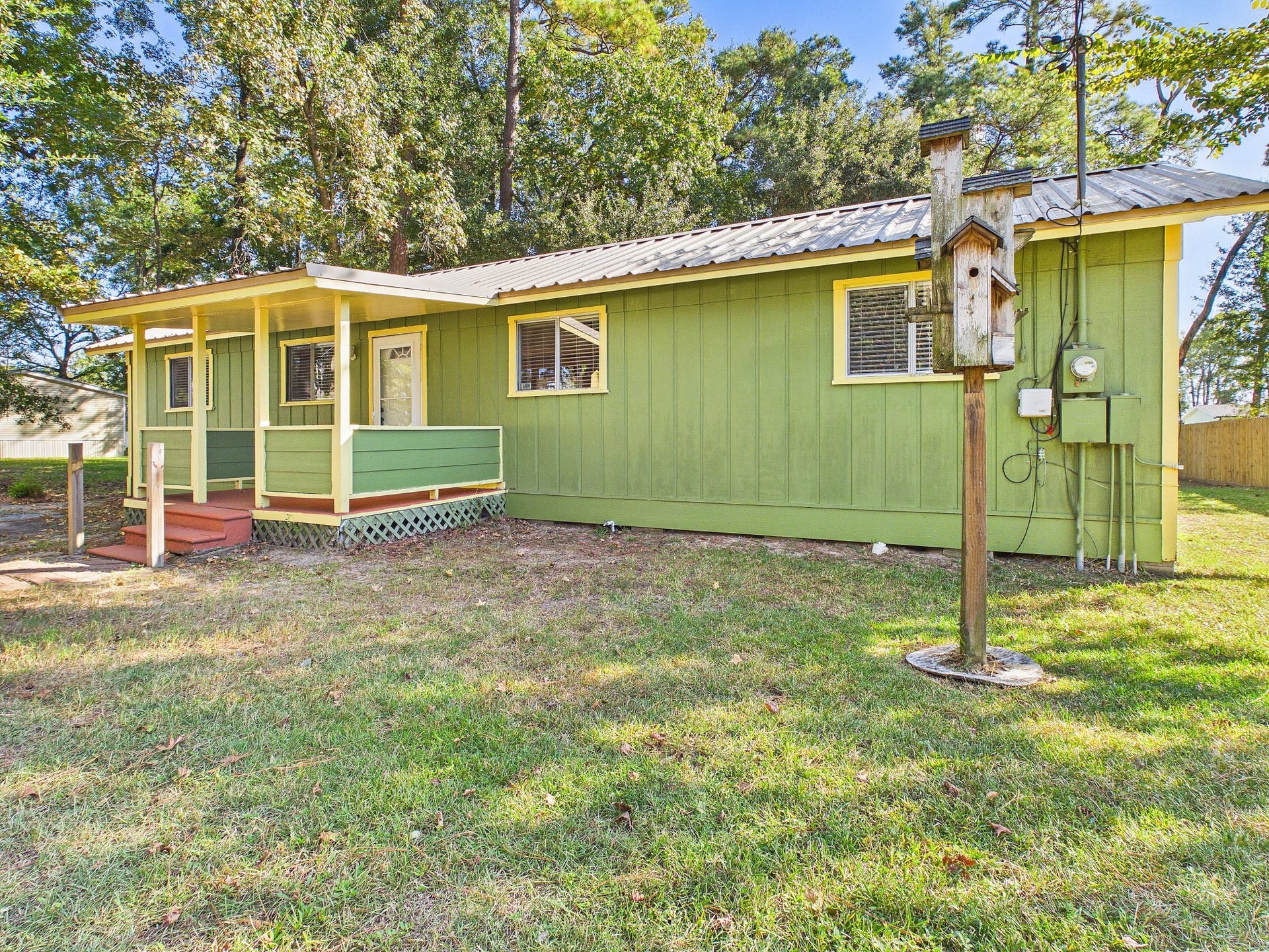 22054 Spears Road, Porter, TX 77365 Charming green cottage with a welcoming front porch, nestled in a serene, wooded setting.