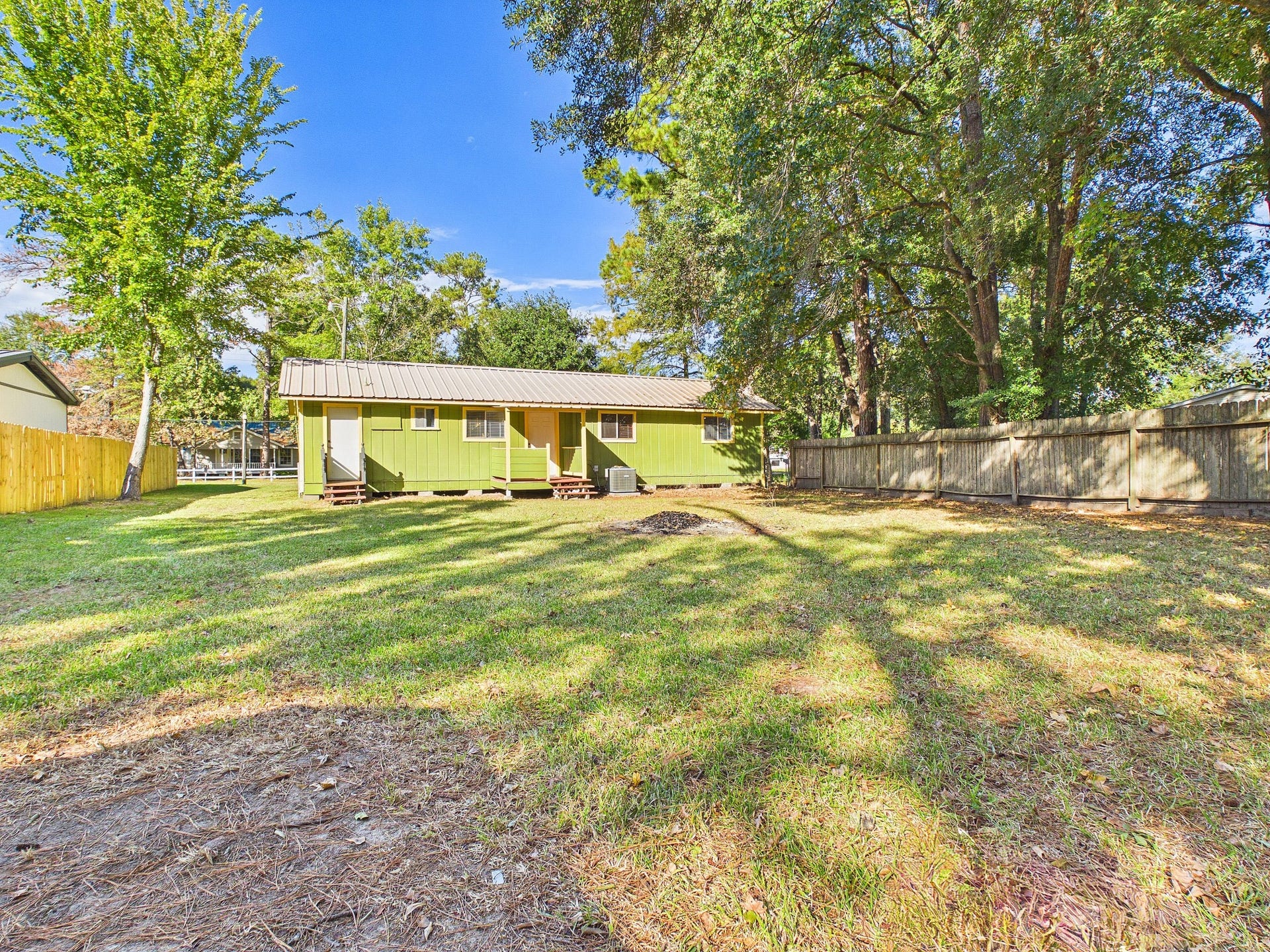 22054 Spears Road, Porter, TX 77365 Expansive backyard with lush greenery and mature trees, perfect for outdoor activities, featuring a charming green house with a welcoming porch.