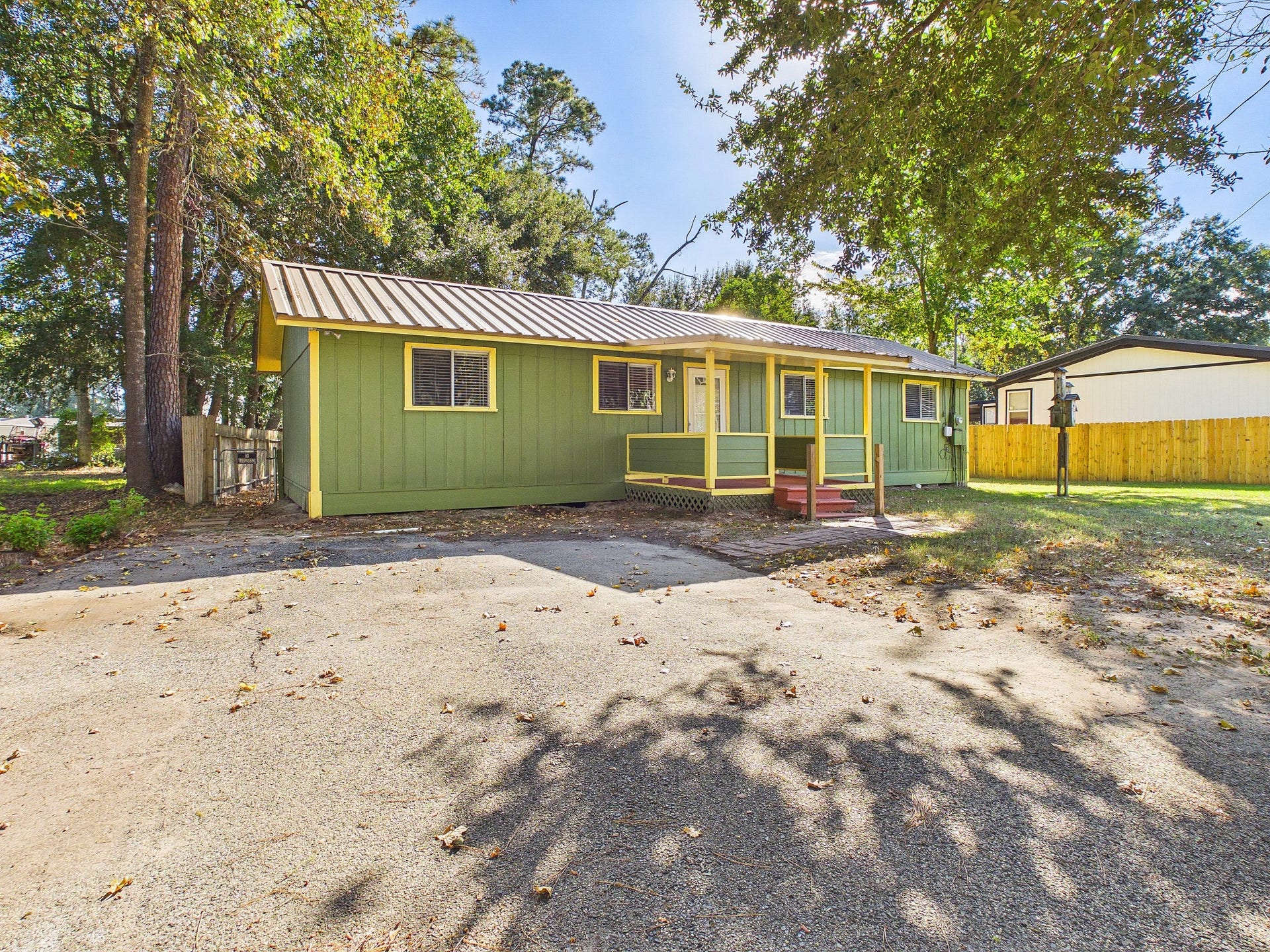 22054 Spears Road, Porter, TX 77365 Charming single-story home with a welcoming front porch, nestled among mature trees, featuring a vibrant exterior and a spacious driveway.