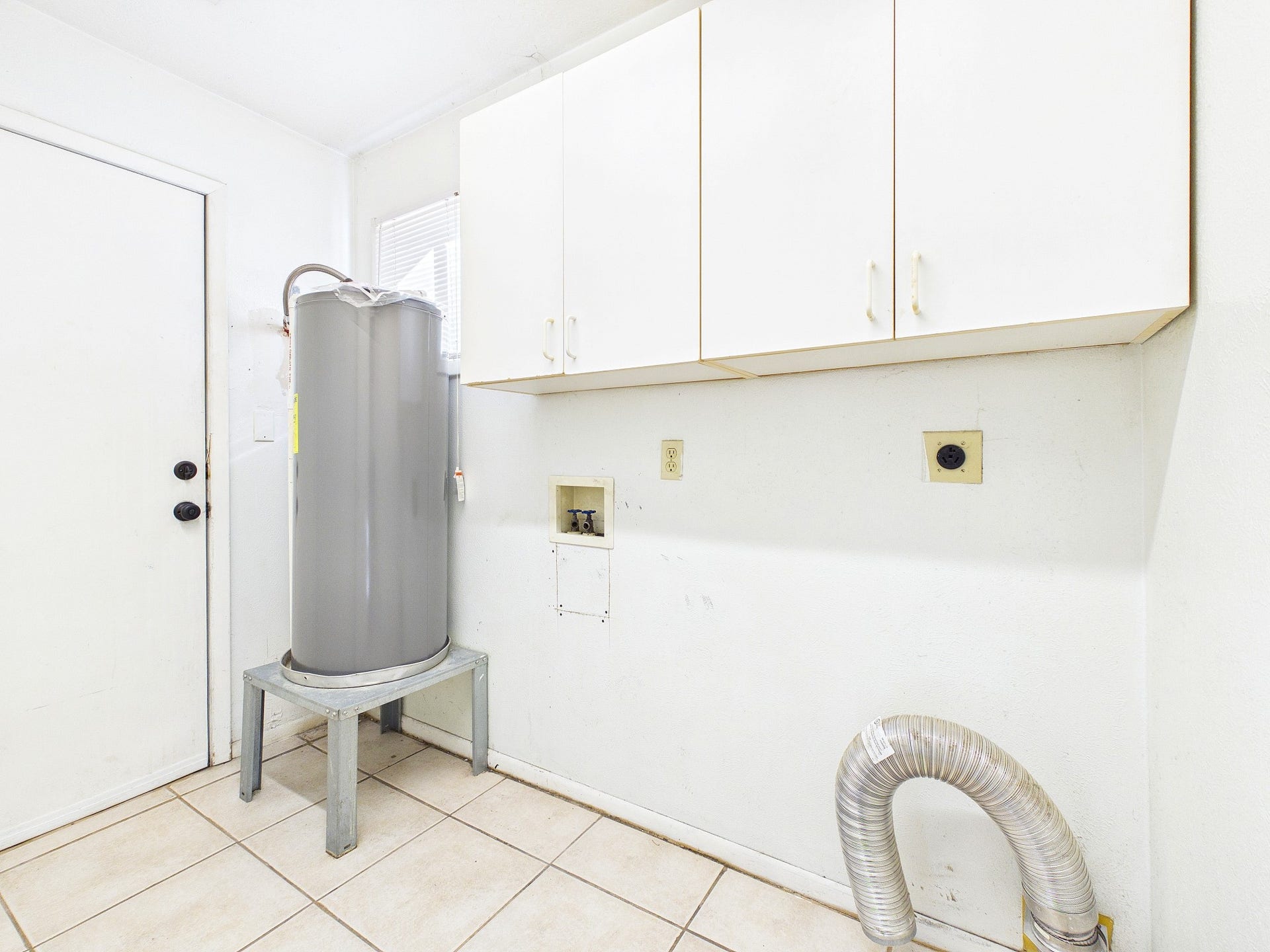 22054 Spears Road, Porter, TX 77365 Utility room equipped with a modern water heater, ample storage cabinets, and connections for laundry appliances, all set on durable tiled flooring.