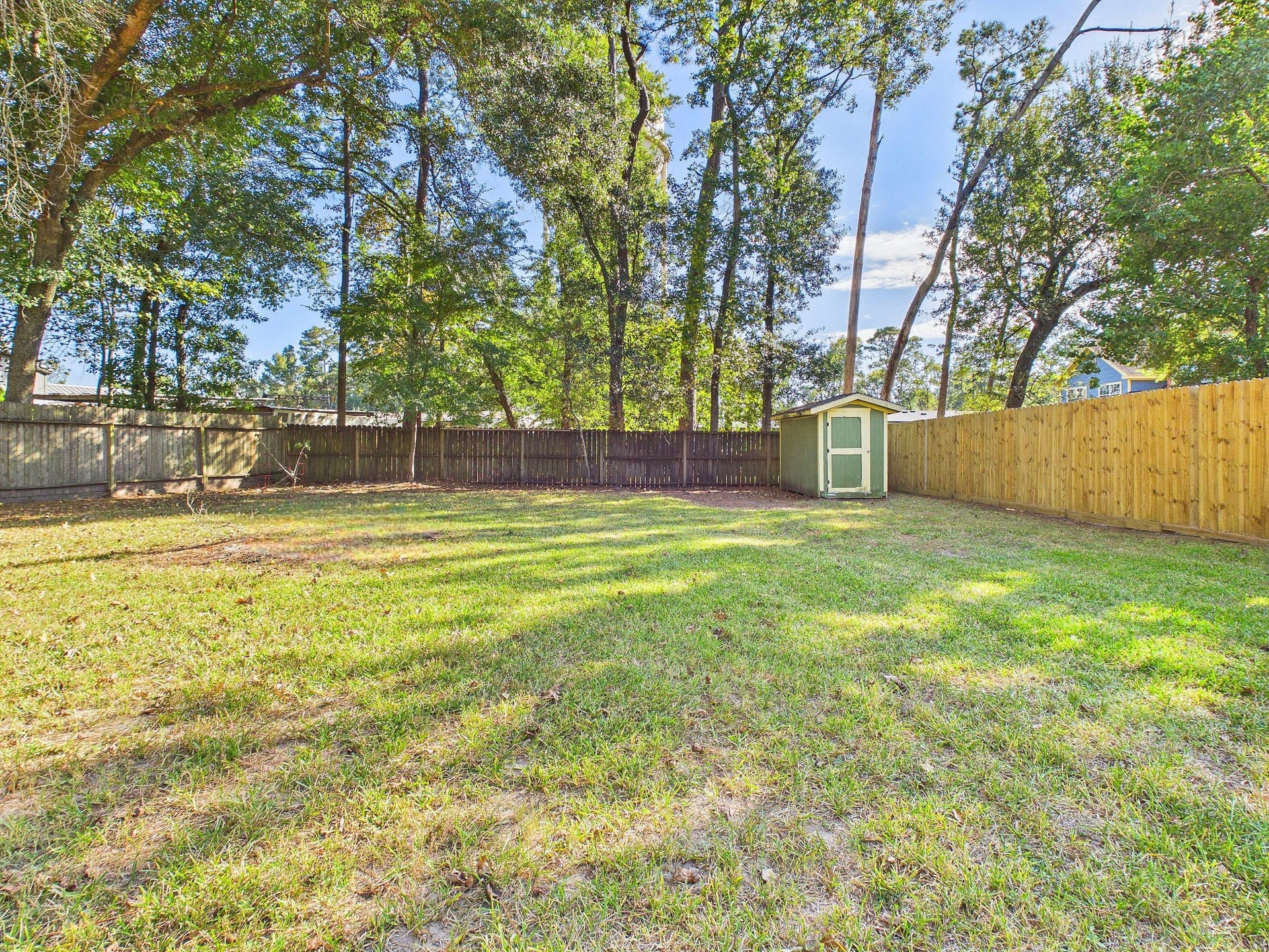 22054 Spears Road, Porter, TX 77365 Expansive backyard with lush greenery, surrounded by a privacy fence, featuring a charming storage shed.