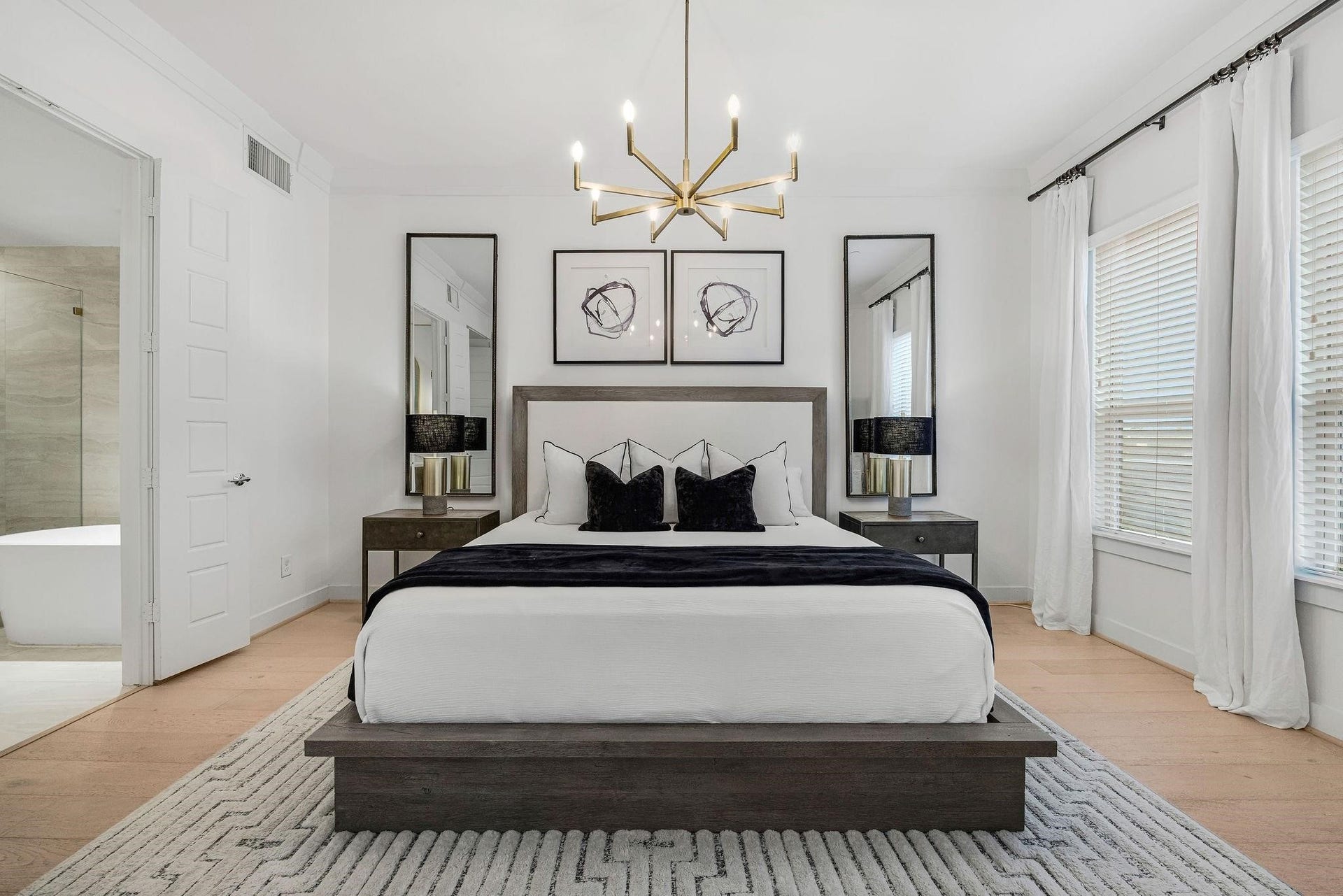 Spacious primary suite with designer lighting, light wood floors, and direct access to the luxurious primary bath.