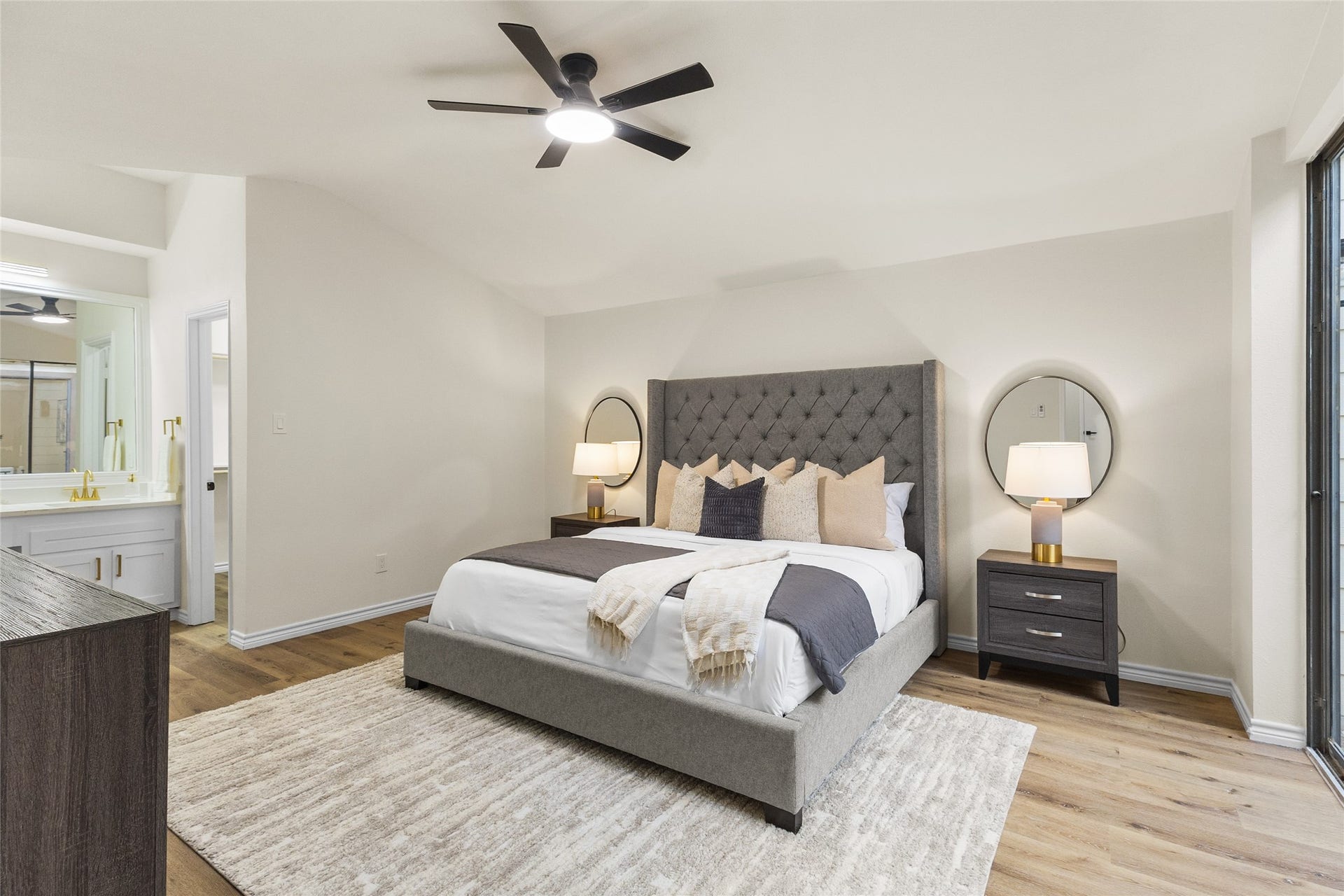 Your spacious primary bedroom features a vaulted ceiling, modern ceiling fan, beautiful wood-look flooring, and sliding glass doors overlooking the courtyard, with convenient access to the ensuite bathroom.