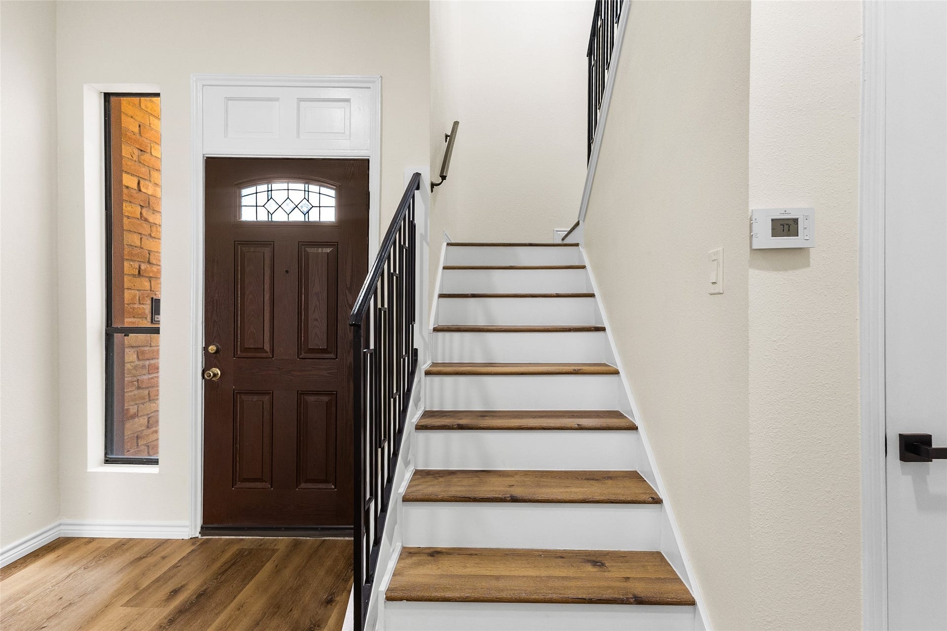 Your welcoming entryway showcases a rich wood front door with decorative glass detailing, wood-look flooring, and a staircase with wood treads and modern black metal railings.