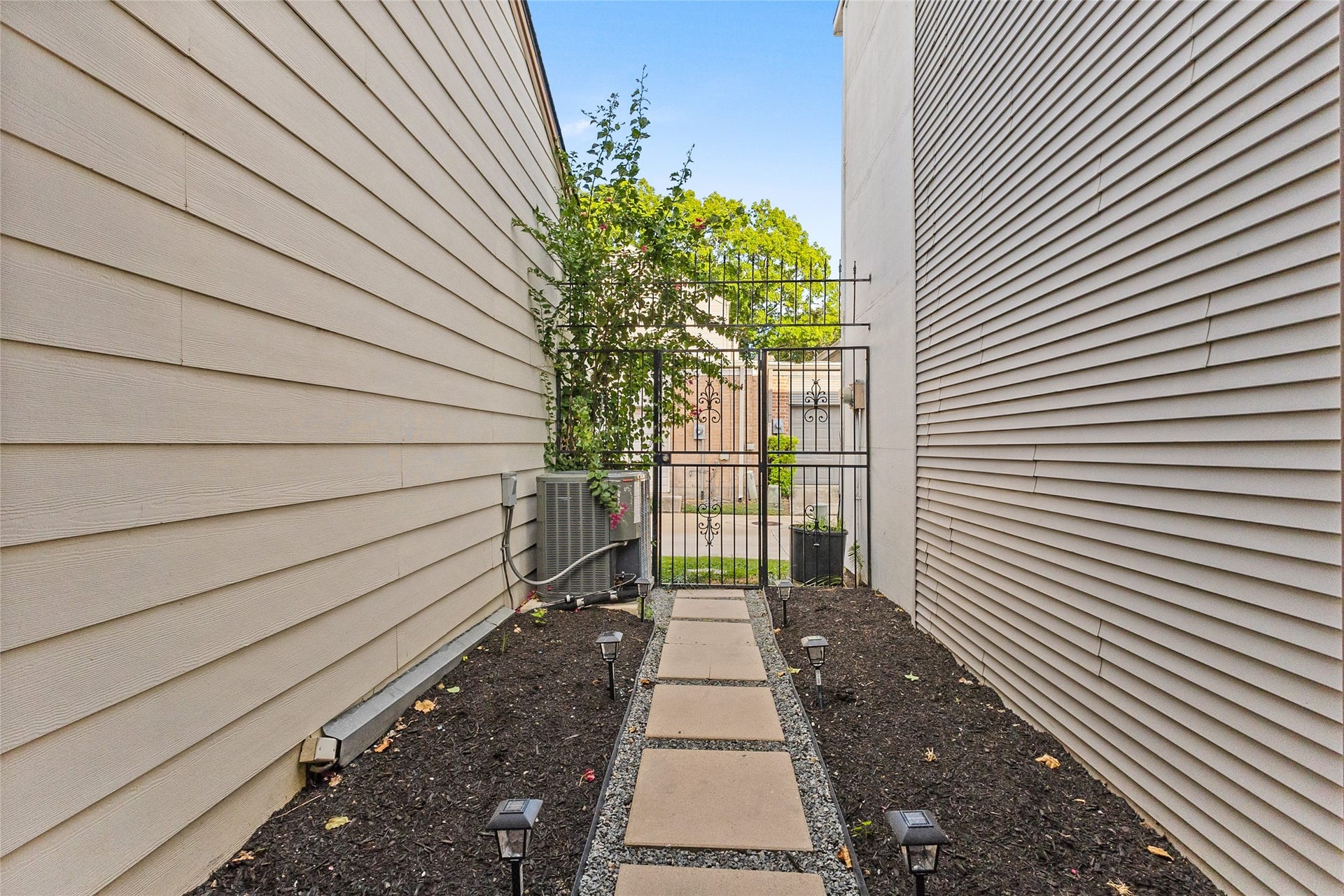 Private outdoor courtyard features a stepping-stone walkway, landscaped garden beds, pathway lighting, and a decorative wrought-iron gate.