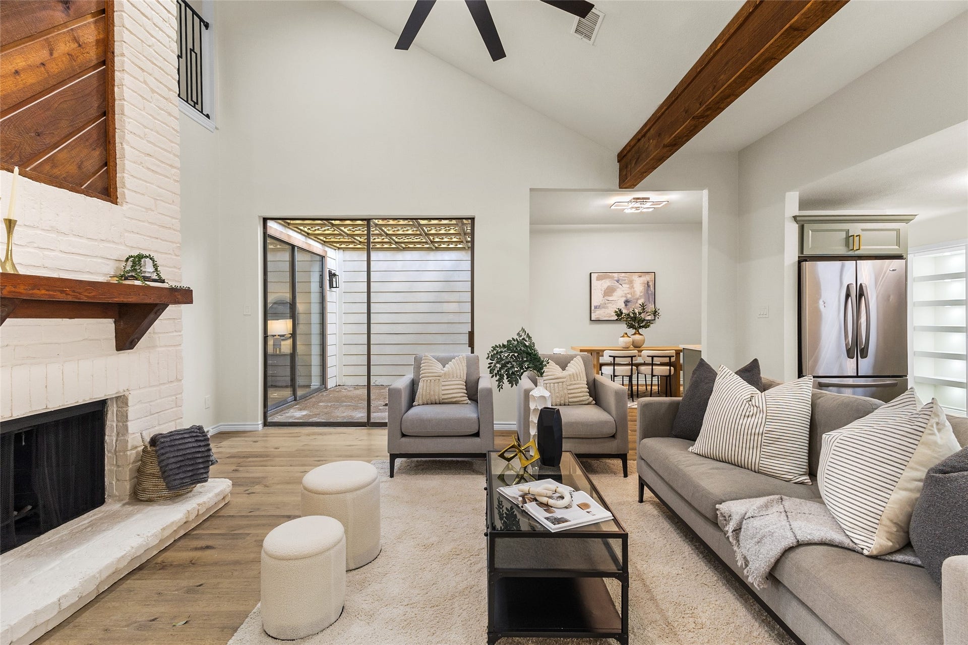 Once again, here is your gorgeous living area showcasing a striking white-painted brick fireplace with a wooden mantel, vaulted ceilings, exposed beams, and sliding glass doors leading to a private atrium.
