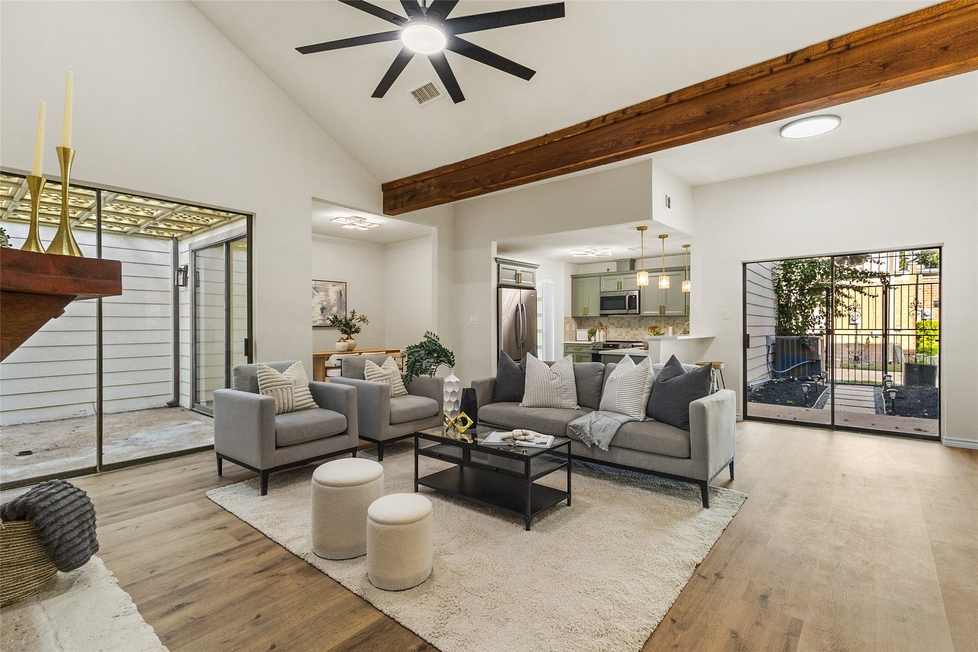 Your living room features soaring vaulted ceilings, exposed wooden beams, a modern ceiling fan, warm wood-look flooring, and large sliding glass doors offering natural light and courtyard views.
