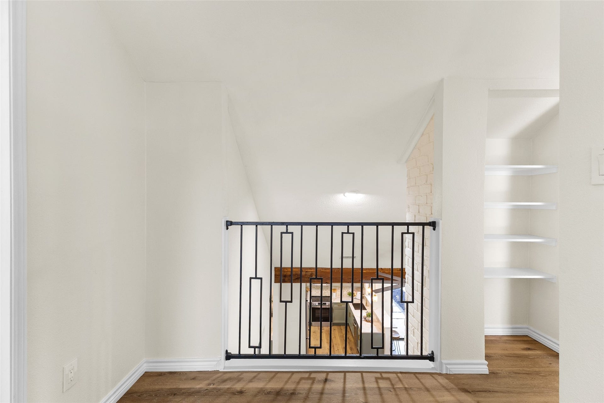 Your stair landing features wood-look flooring, a decorative black metal railing, a white-painted brick accent wall, and built-in shelving.