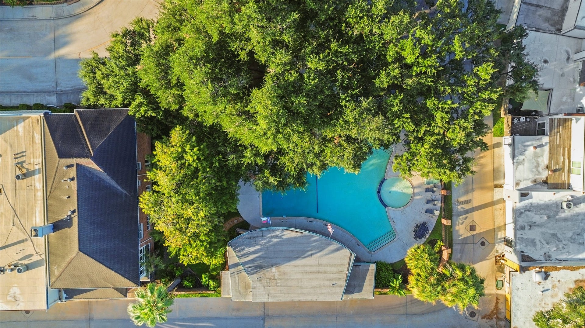 This beautiful aerial view captures the communities outdoor swimming pool surrounded by mature trees.