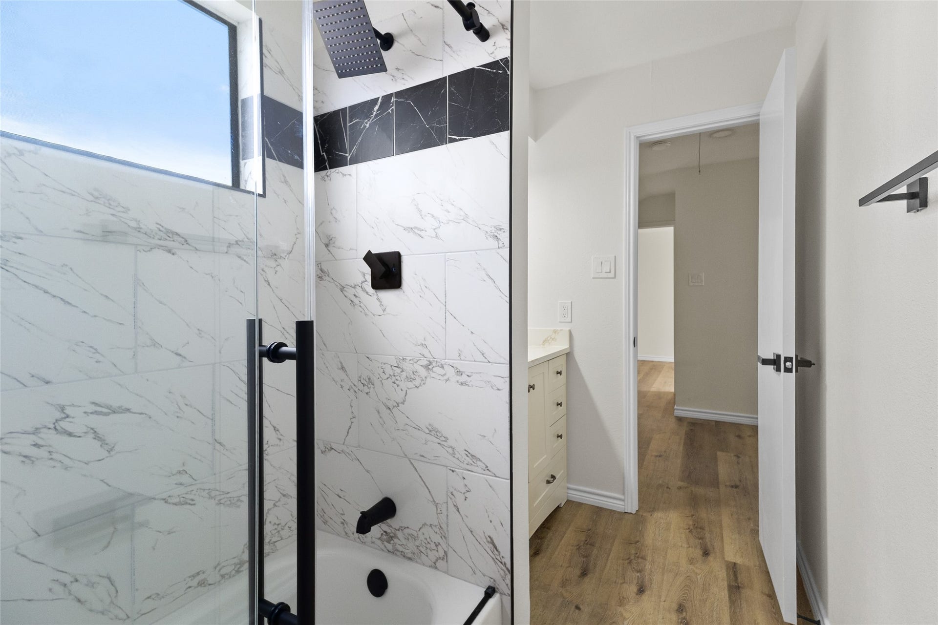 Your secondary bathroom upstairs features a shower/tub combo with striking marble-look tile surrounds with contrasting black accents, a rainfall showerhead, and a single vanity with plenty of storage.