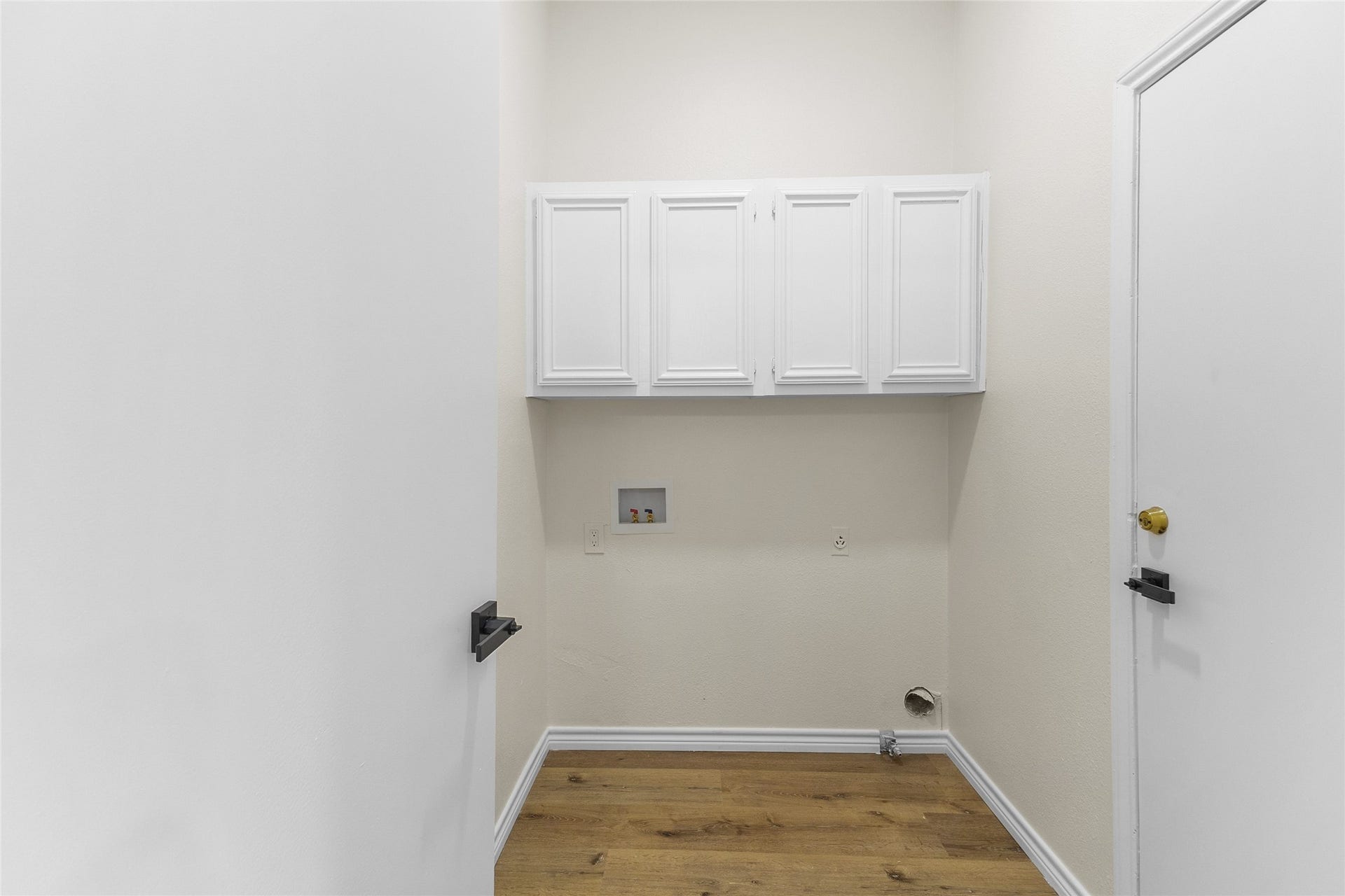 Loctaed off the kitchen, your convenient laundry room features white overhead storage cabinets, washer and dryer hookups, crisp neutral walls, and warm wood-look flooring for a clean and functional space. Garage access to the right.
