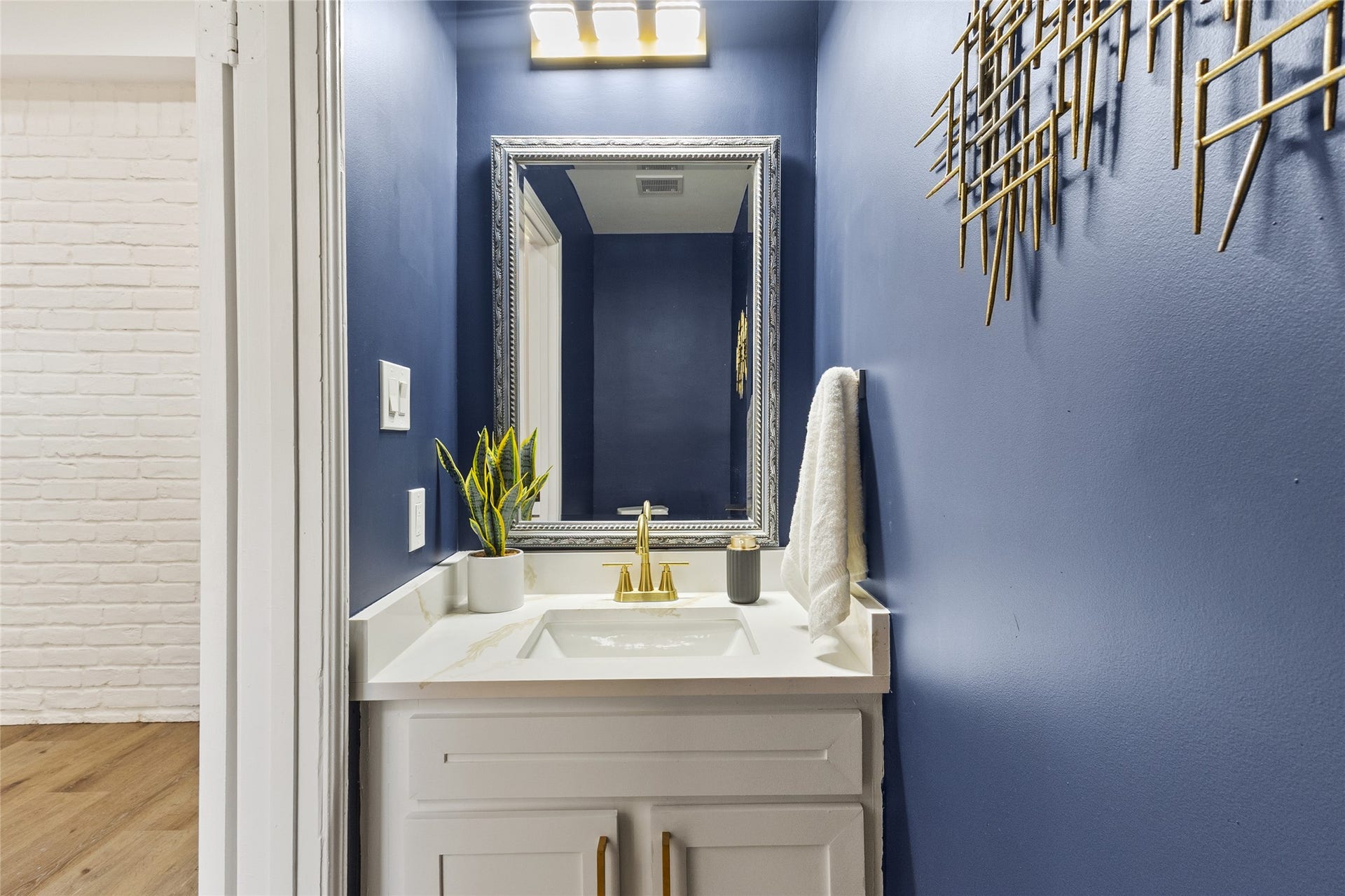 Located at the front of the home, your stylish powder room showcases rich navy-blue walls, a white vanity with gold fixtures, a decorative framed mirror, and modern lighting.