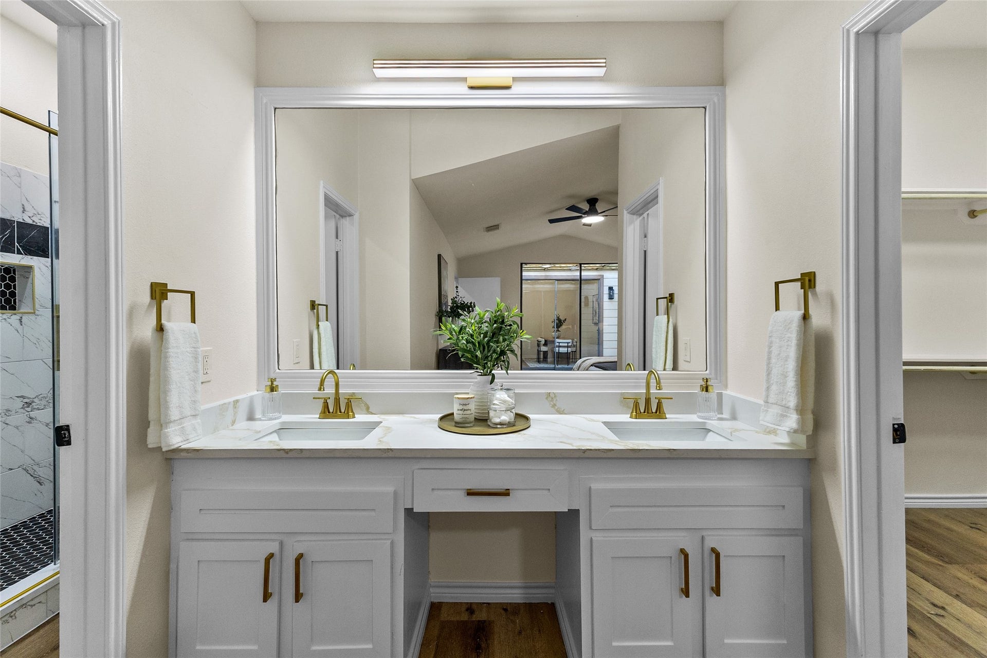 Your stylish primary bathroom features a double-sink vanity with elegant gold fixtures, a large framed mirror, and modern lighting. Just off the vanity, a spacious walk-in shower showcases marble-look tile, dual rainfall showerheads with handheld sprayers, a built-in bench, and two tiled niches for a spa-like experience.
