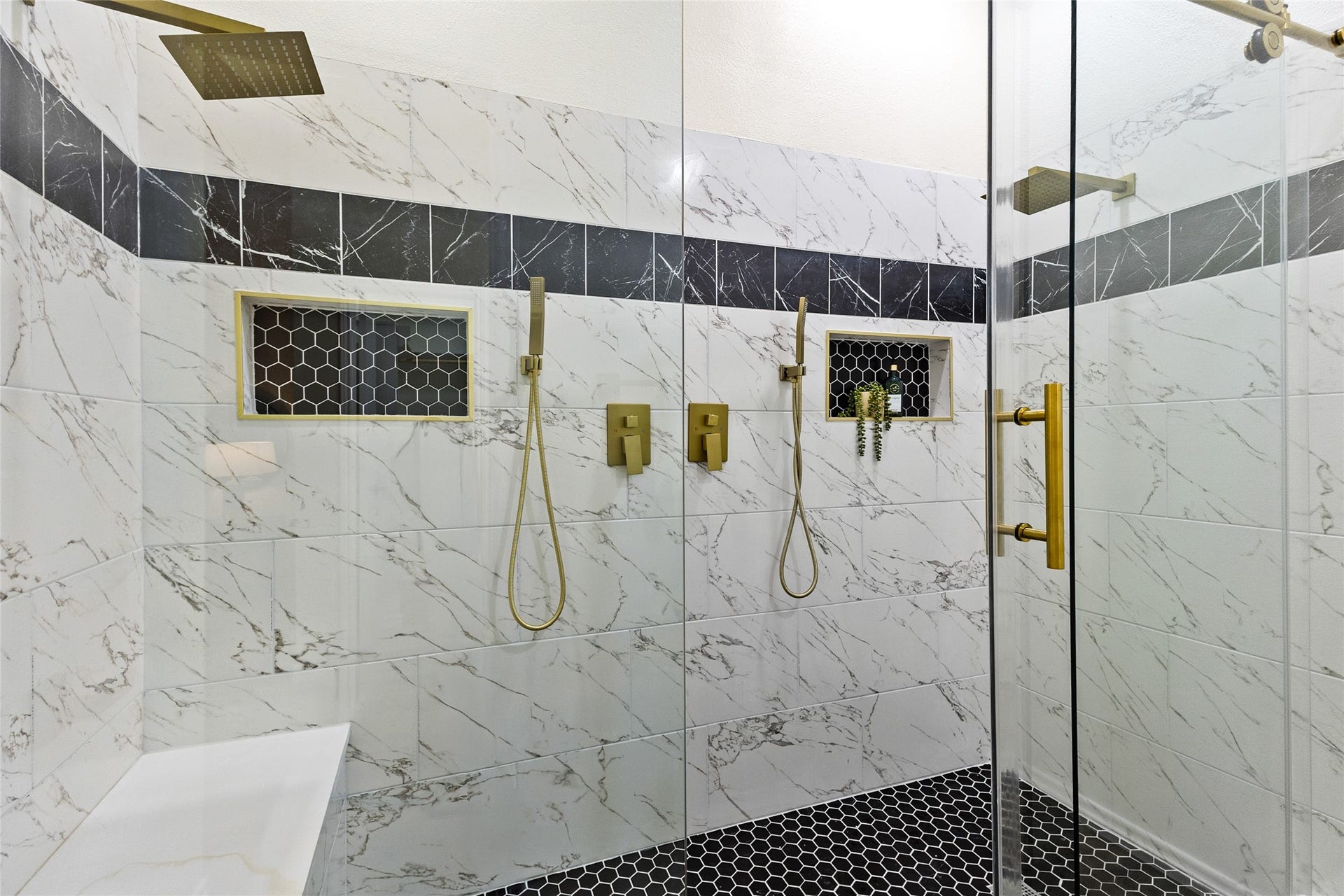 Another look at your luxurious walk-in shower featuring marble-look tile, contrasting black accents, dual rainfall showerheads, handheld sprayers, built-in niches, and elegant gold fixtures.