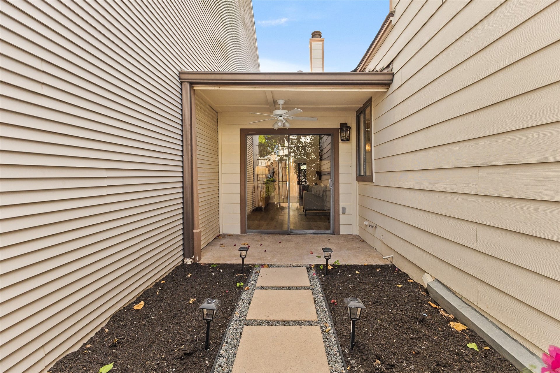Your charming private courtyard features a stepping-stone pathway, decorative gravel, landscaped beds, and a covered patio with a ceiling fan and sliding glass doors.