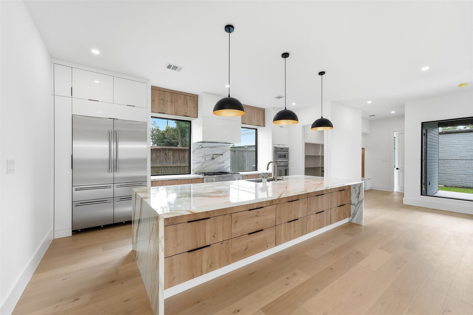 519 W 30th Street, Houston, TX 77018 A showstopping kitchen centered around an oversized waterfall island with dramatic stone detailing, warm wood cabinetry, sleek black hardware, and abundant storage. THERMADOR appliances, and expansive windows complete the clean, modern design.