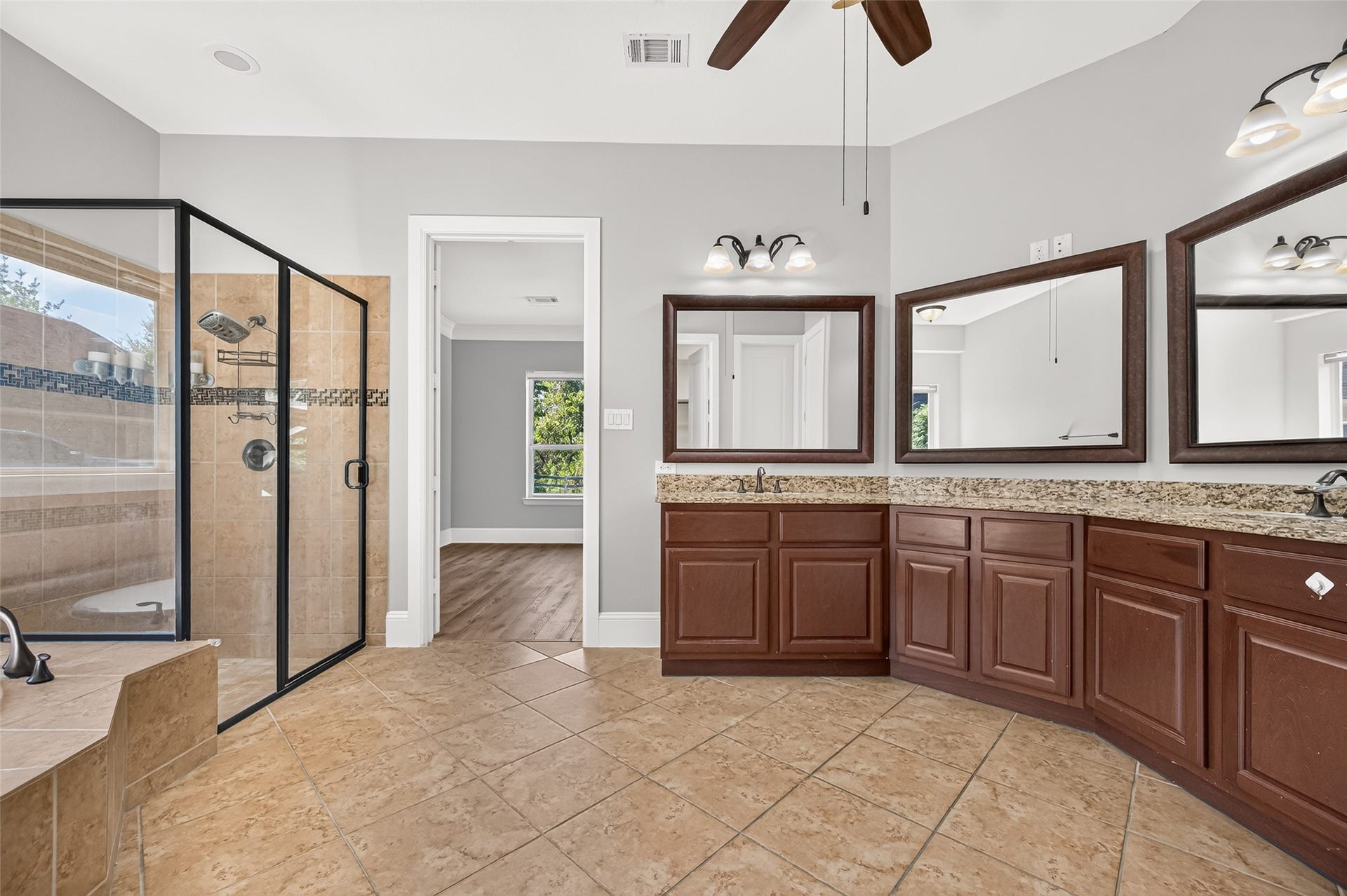 5119 Water Oak Crescent, Fulshear, TX 77441 Spa-like primary bath! Indulge in the deep corner soaking tub with elegant tile detailing. Features a massive granite-topped vanity with dual sinks, rich wood cabinetry, a large framed mirror, stylish lighting, and a massive walk-in layout.