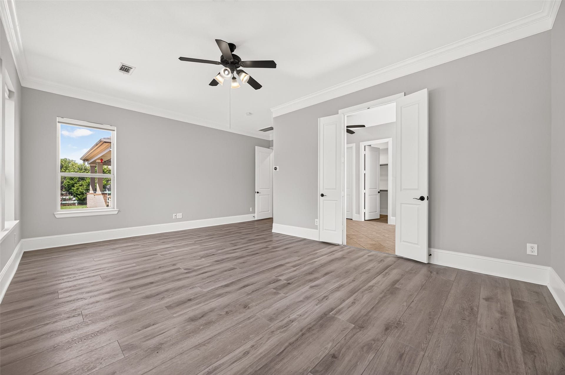 5119 Water Oak Crescent, Fulshear, TX 77441 Serene primary suite retreat! This spacious bedroom boasts stylish, modern wood-look flooring, elegant crown molding, a classic ceiling fan, and a wall of large windows overlooking the lush, private backyard space.
