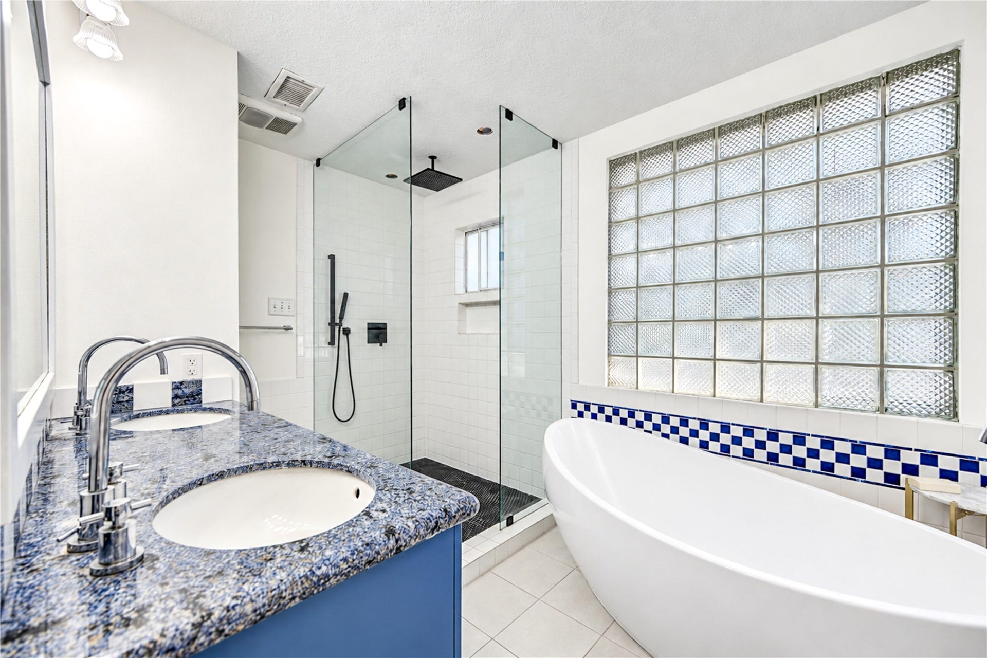 11423 Inwood Drive, Houston, TX 77077 Indulge in a little everyday luxury! This beautifully renovated primary ensuite bath features a stunning freestanding soaking tub framed by glass block windows, creating a bright and relaxing retreat. The spacious walk-in shower with frameless glass enclosure, stylish tilework and striking blue accents adds a fresh designer touch. Whether starting your morning or unwinding after a long day, this spa-inspired sanctuary makes every moment feel special!