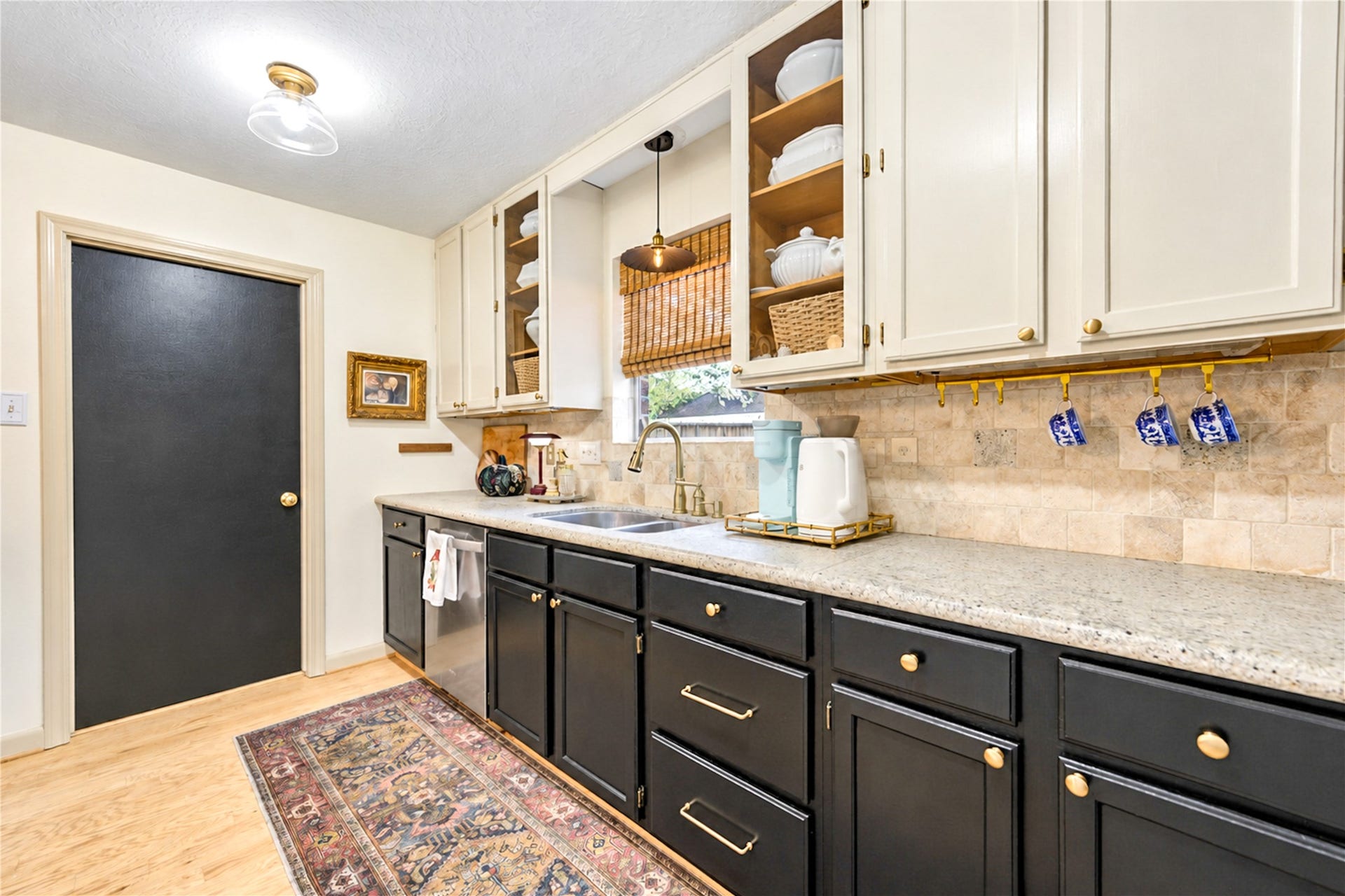 11423 Inwood Drive, Houston, TX 77077 Style meets everyday convenience in this thoughtfully designed kitchen! Crisp white upper cabinetry contrasts beautifully with rich dark lower cabinets, while granite countertops and a travertine backsplash add timeless appeal. Charming display shelves, warm wood floors and designer lighting bring personality to the space, making everything from morning meal prep to evening entertaining a pleasure!