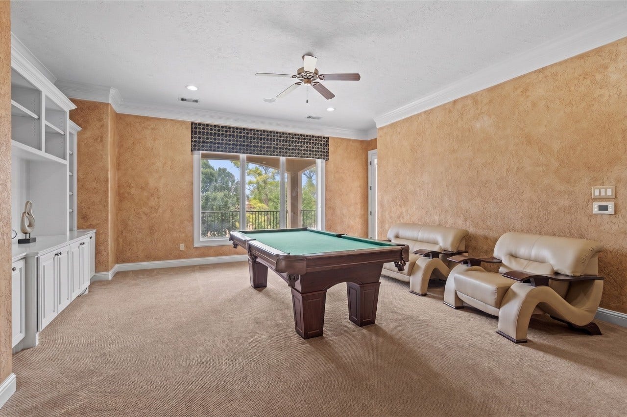 The game room featuring a billiards area, custom built-in cabinetry, and large windows overlooking the surrounding greenery.