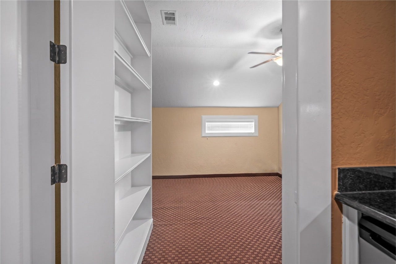Bonus hidden room behind the book shelf featuring built-in shelving, recessed lighting, patterned carpeting, and a small window for natural light.