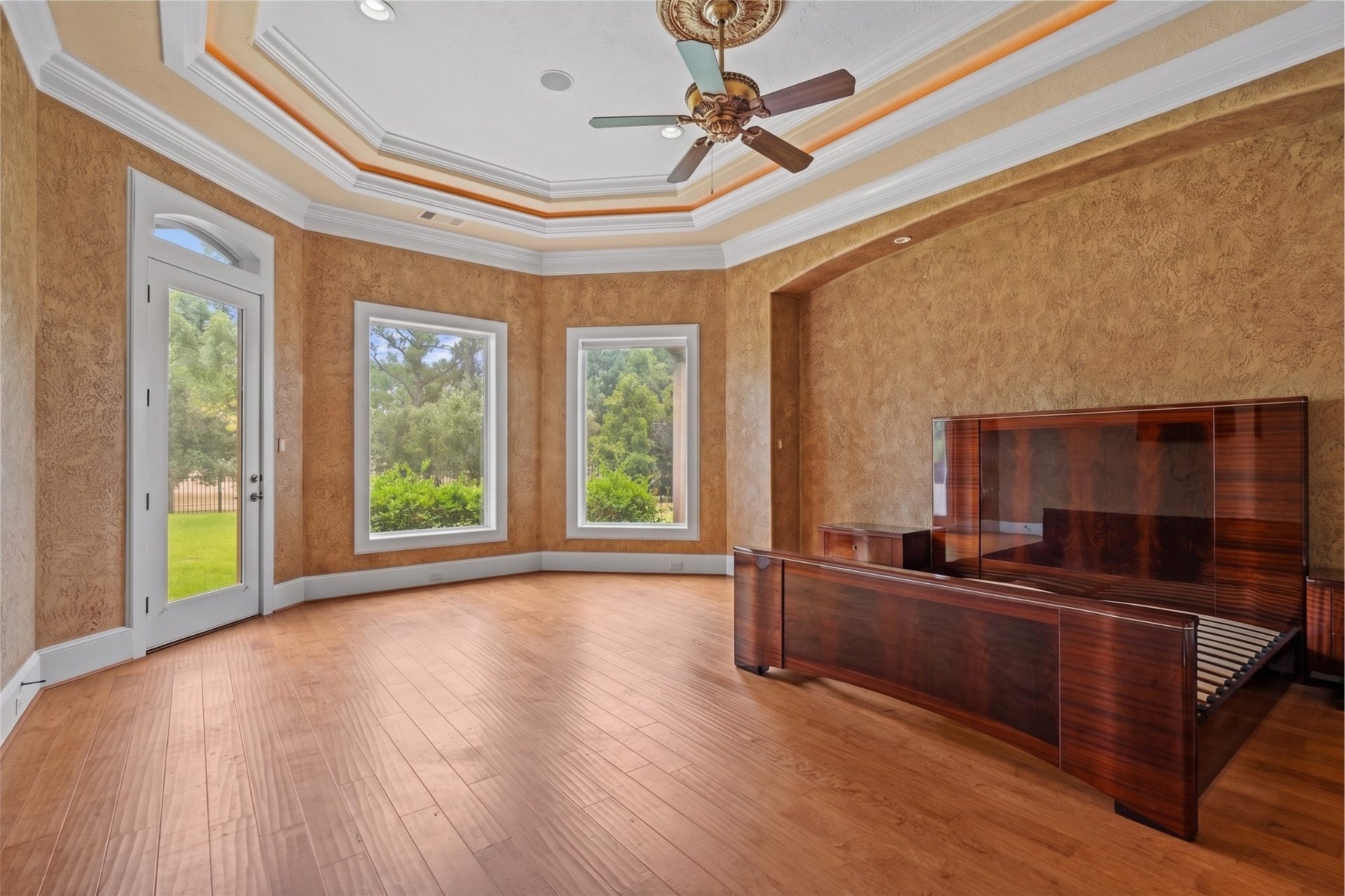 Grand primary suite showcasing an intricate coffered ceiling, rich wood flooring, expansive windows, and direct access to the backyard.
