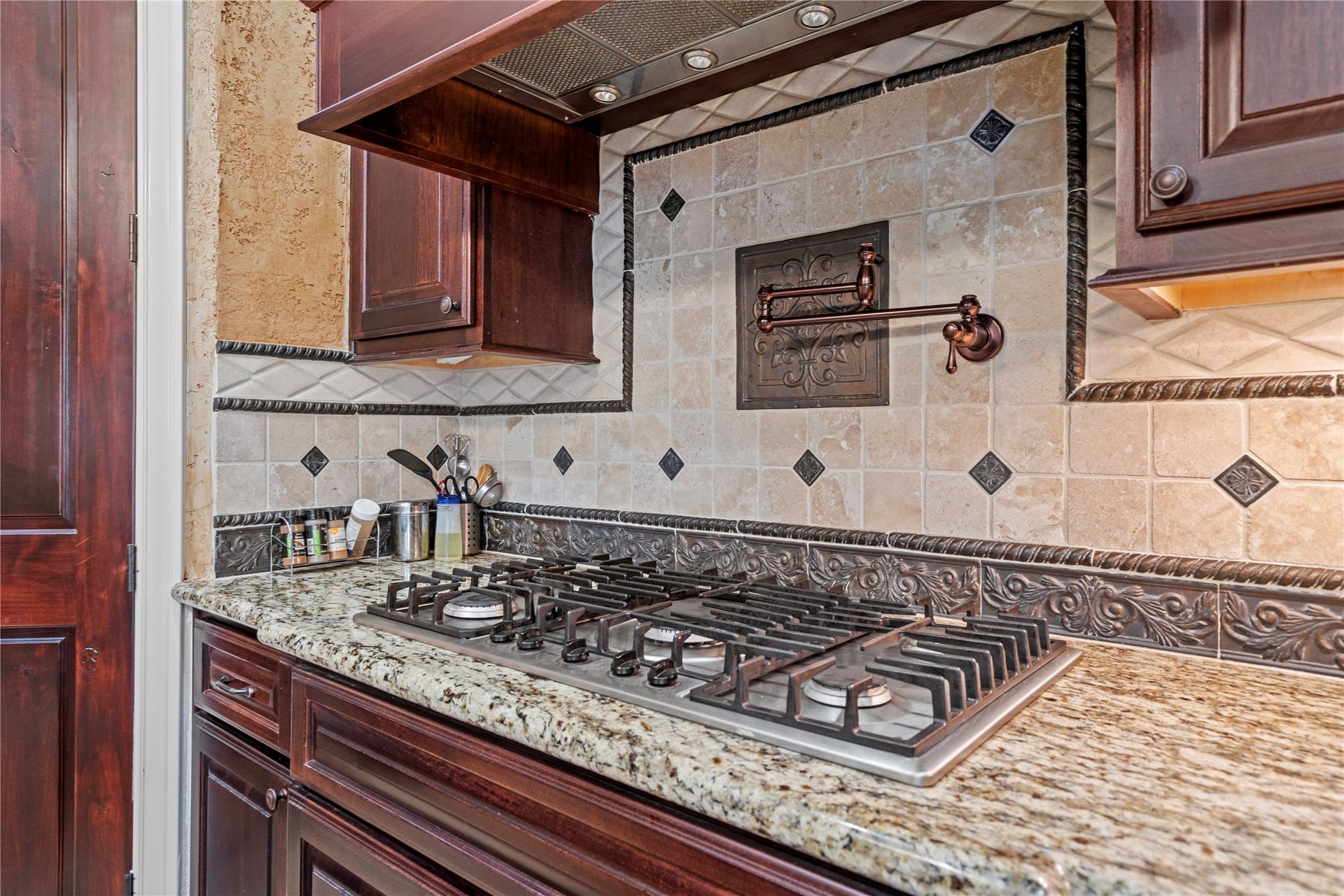 Chef-inspired cooktop area features a pot filler, professional gas range, detailed tile backsplash, granite surfaces, and rich custom cabinetry.