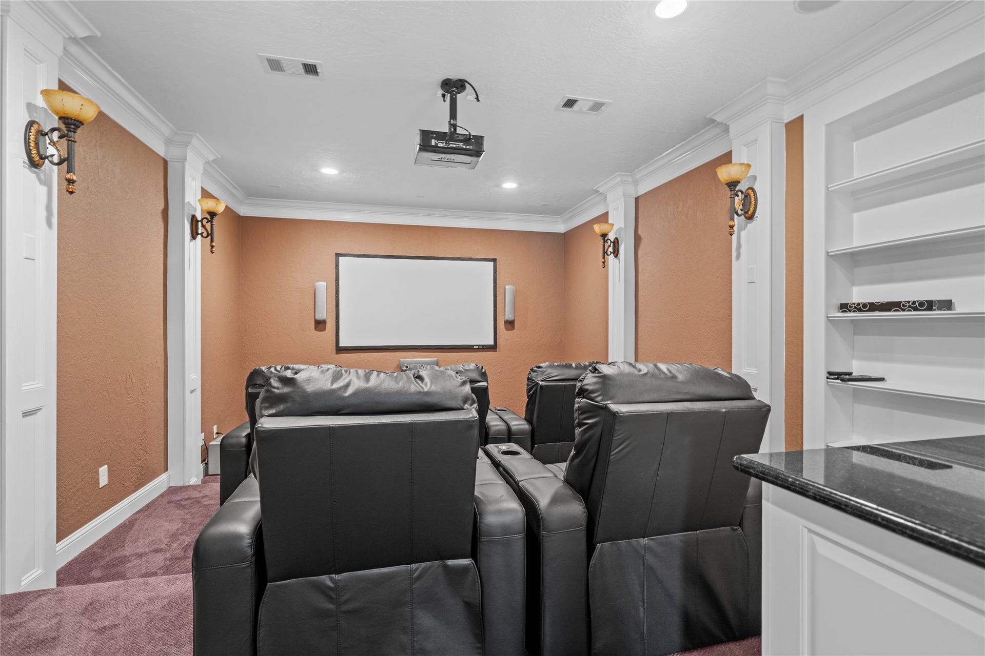 Private home theater featuring tiered seating, a projection screen, built-in shelving, and sophisticated architectural detailing for an immersive entertainment experience.