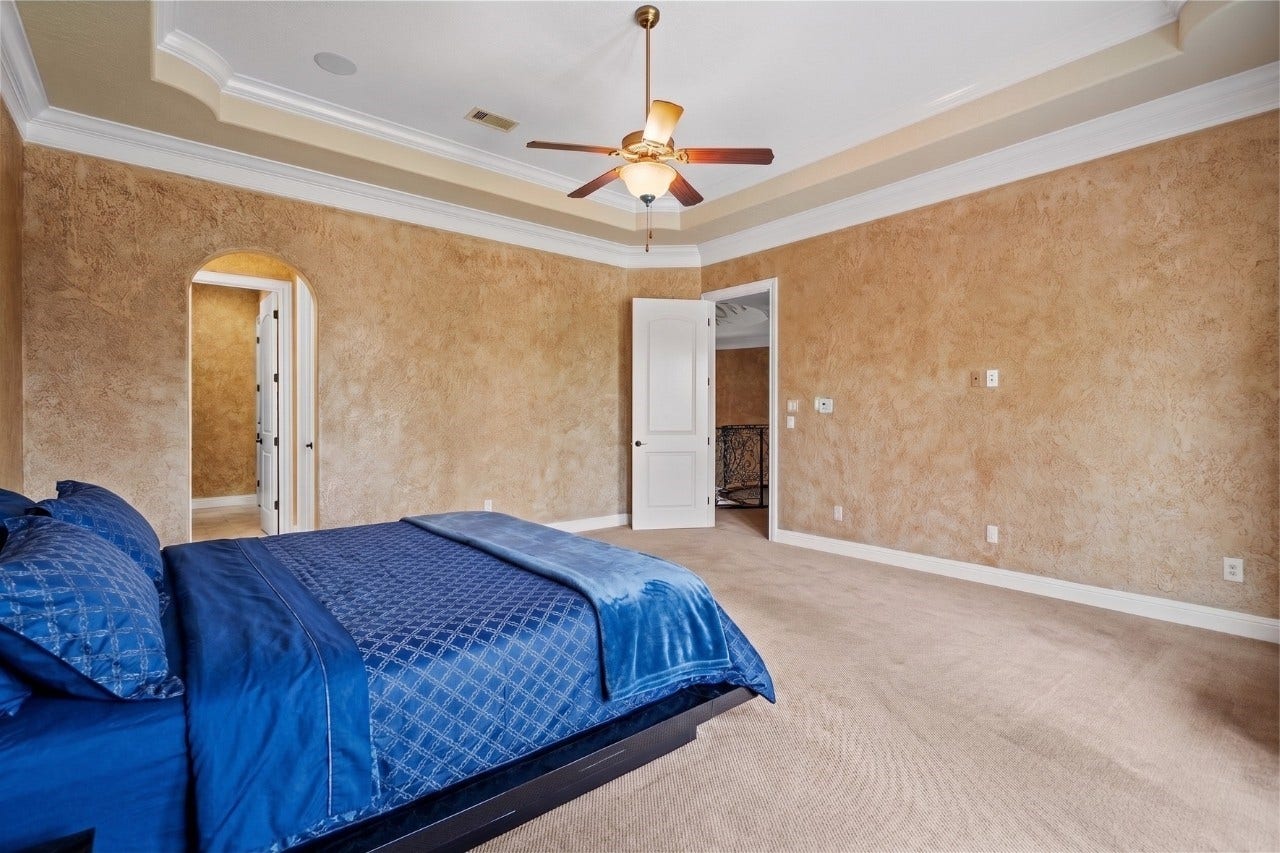 Forth Bedroom featuring a tray ceiling, ceiling fan, arched doorway, and ample room for additional seating or furnishings.