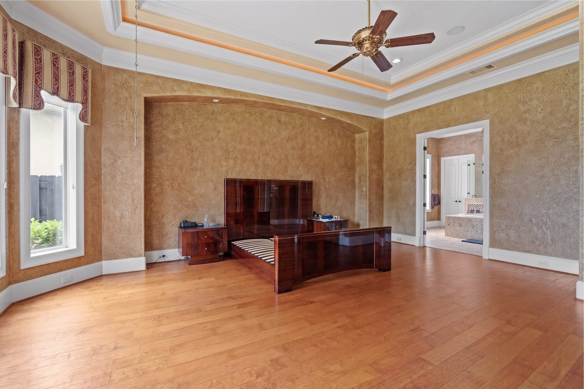 Expansive primary suite highlights an illuminated tray ceiling, warm hardwood flooring, a graceful arched alcove, and seamless access to the luxurious bath.