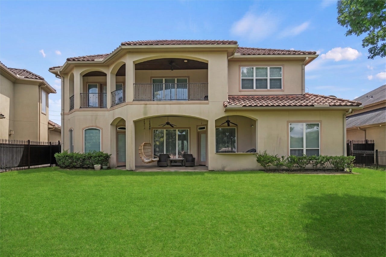 Wide rear exterior view highlighting the expansive backyard, covered patio, upper-level balcony, no back neighbors, and distinctive arched architecture.