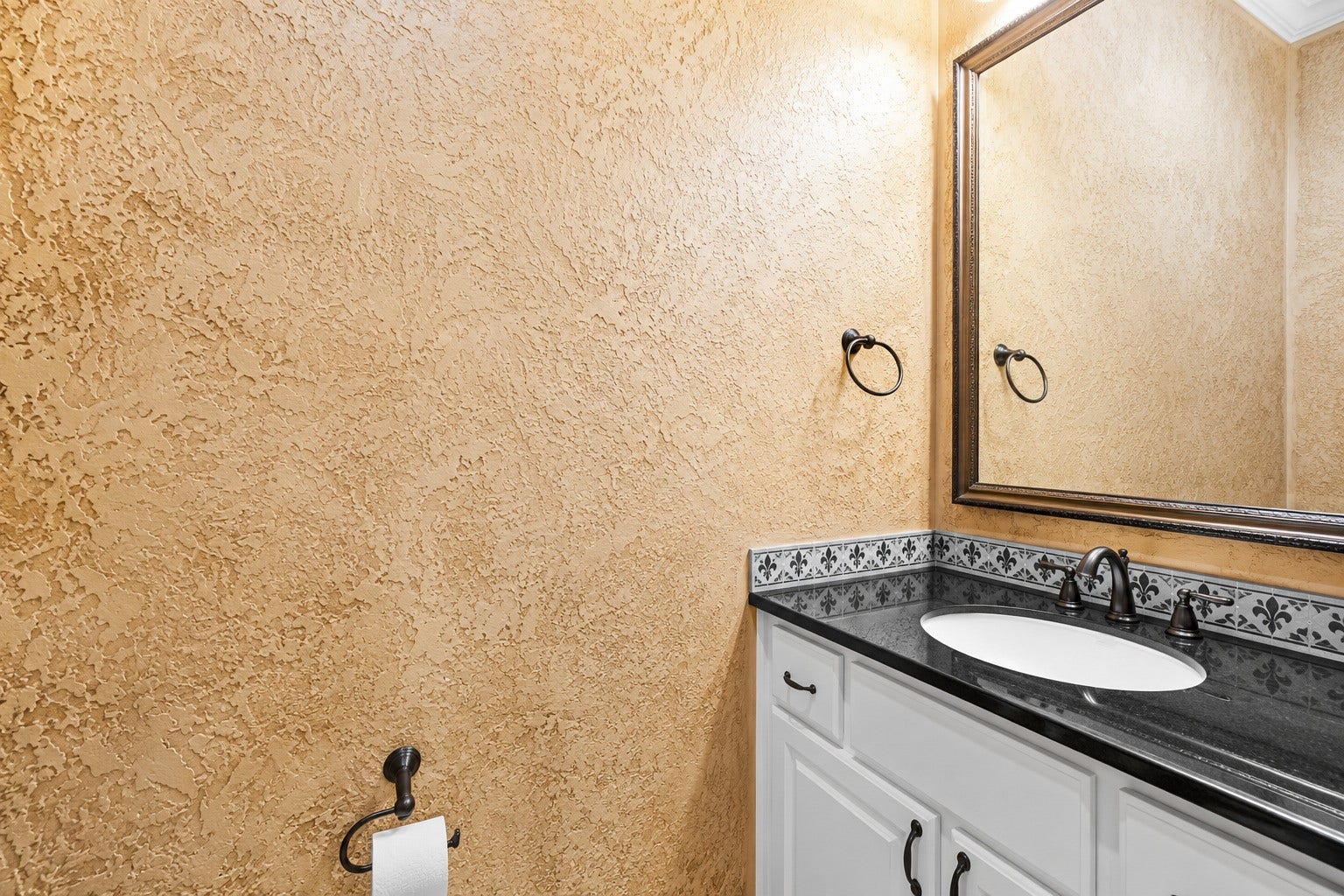 Charming powder room featuring a granite-topped vanity, decorative tile backsplash, framed mirror, and richly textured walls.