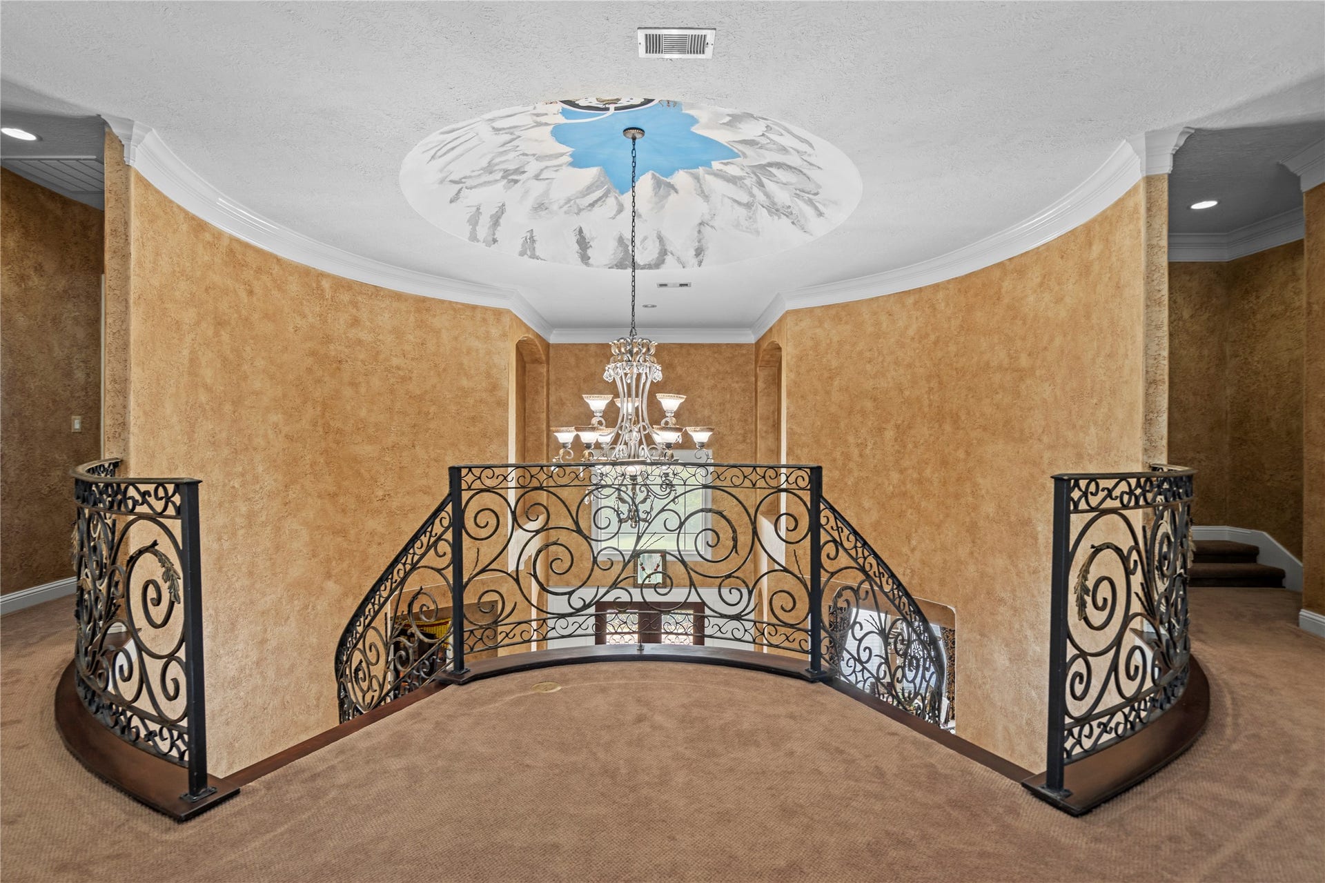 Elegant second-floor landing overlooking the grand foyer, featuring wrought-iron railings, a statement chandelier, custom painted dome and distinctive architectural details.