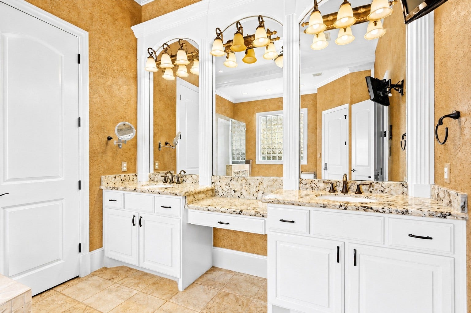 Primary bath vanity features dual sinks, granite countertops, extensive cabinetry, and grand framed mirrors with refined lighting.