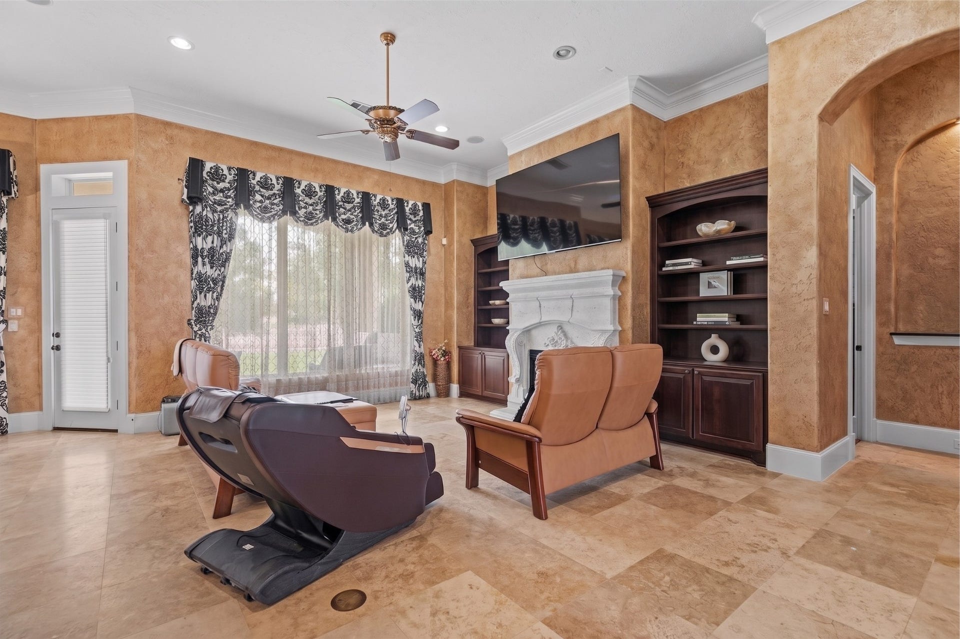Living area featuring an ornate stone fireplace, custom built-in cabinetry, and windows that fill the space with natural light.
