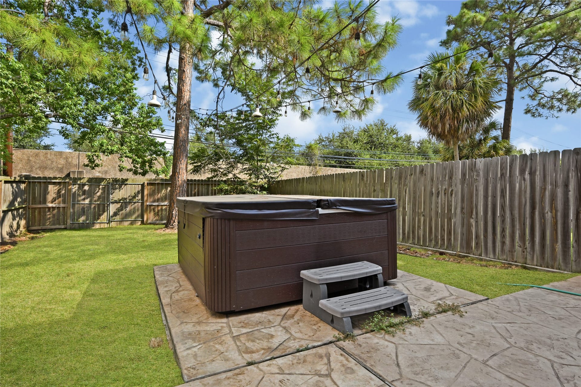2607 Sailboat Drive, Houston, TX 77058 Experience relaxation in this private backyard featuring a luxurious hot tub, surrounded by lush greenery and a charming wooden fence for ultimate seclusion.