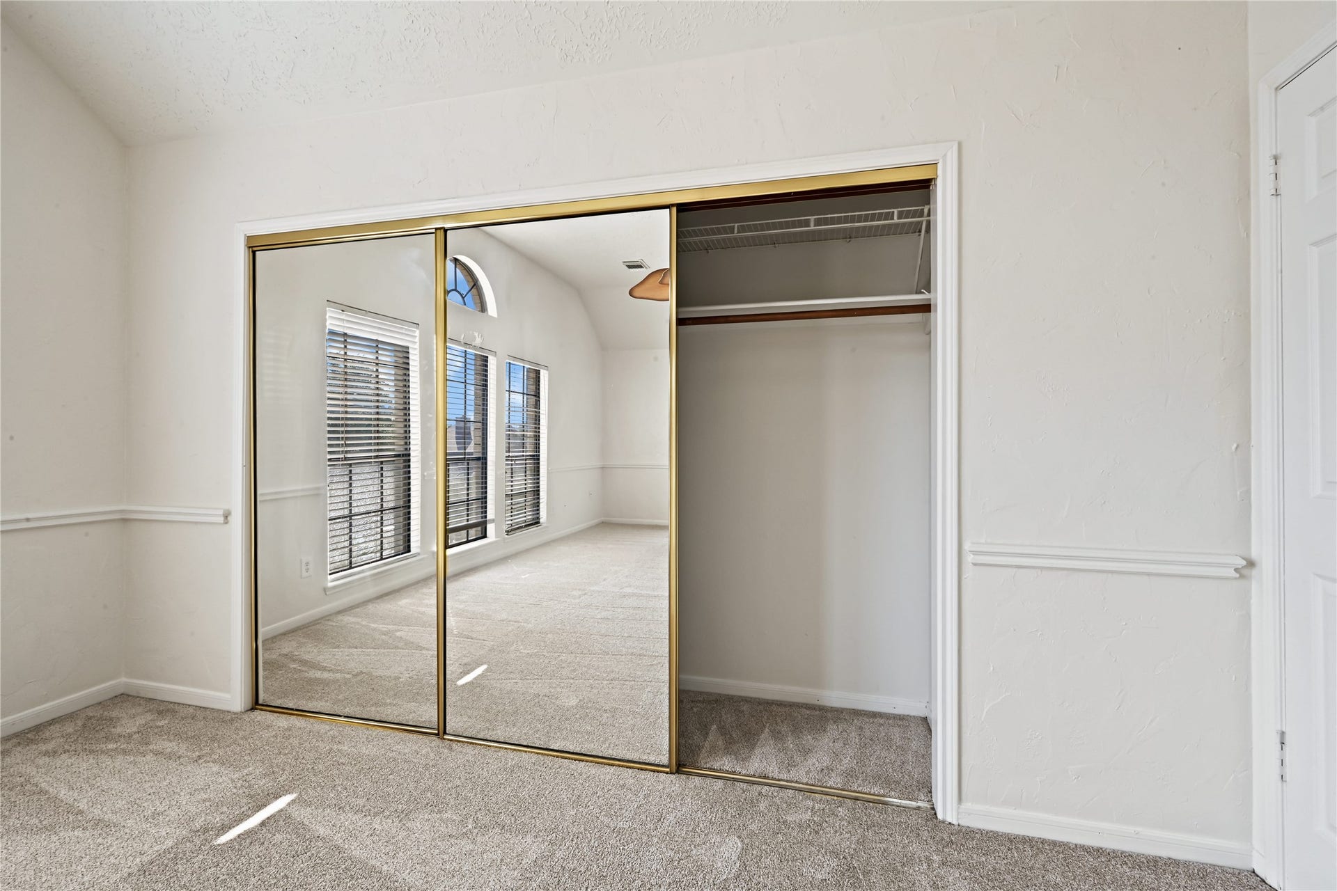 2607 Sailboat Drive, Houston, TX 77058 Spacious bedroom featuring a large mirrored closet, plush carpeting, and abundant natural light through arched windows.